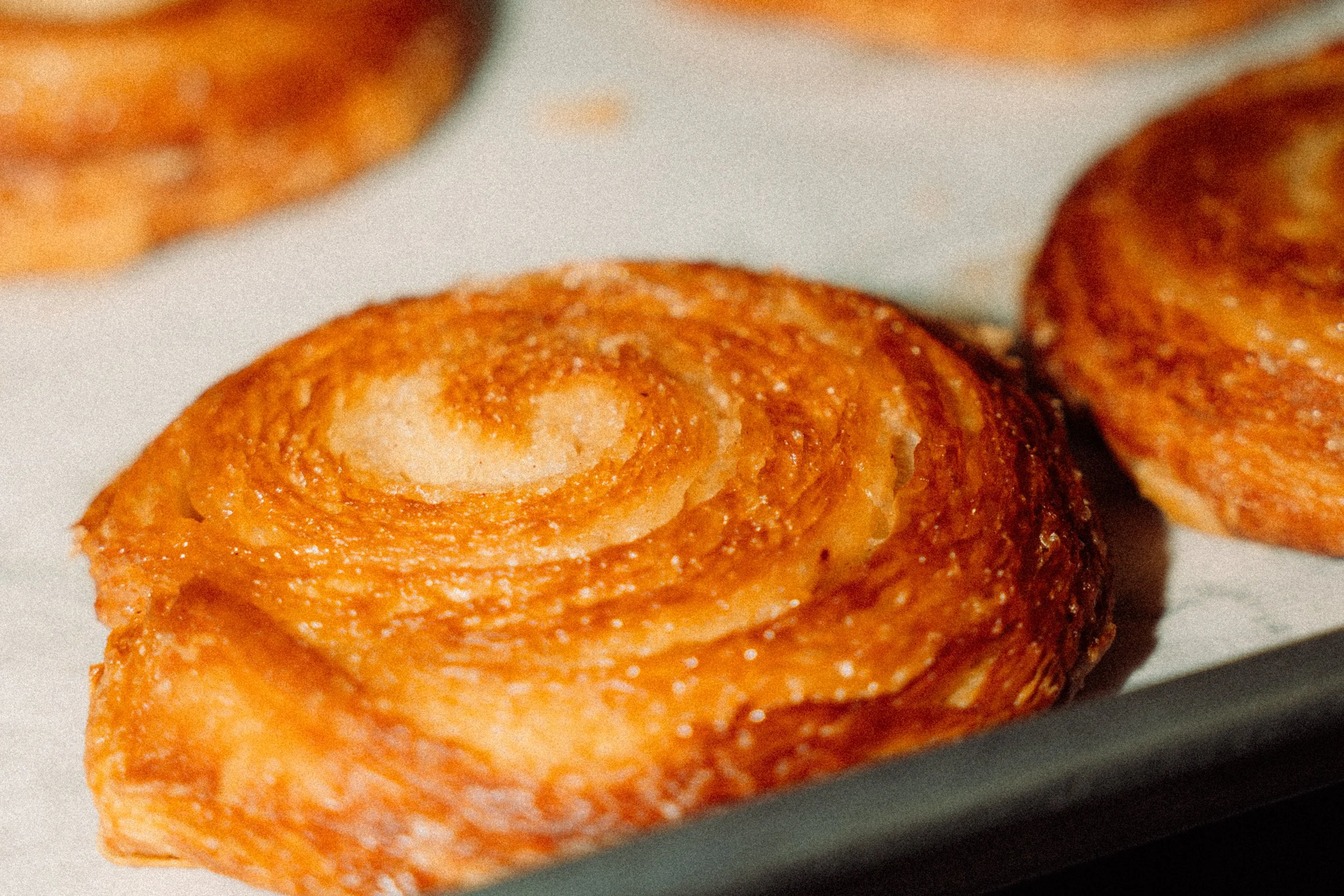 Close-up of a golden-brown, crispy fried roll with a swirled dough pattern, placed on a white surface.