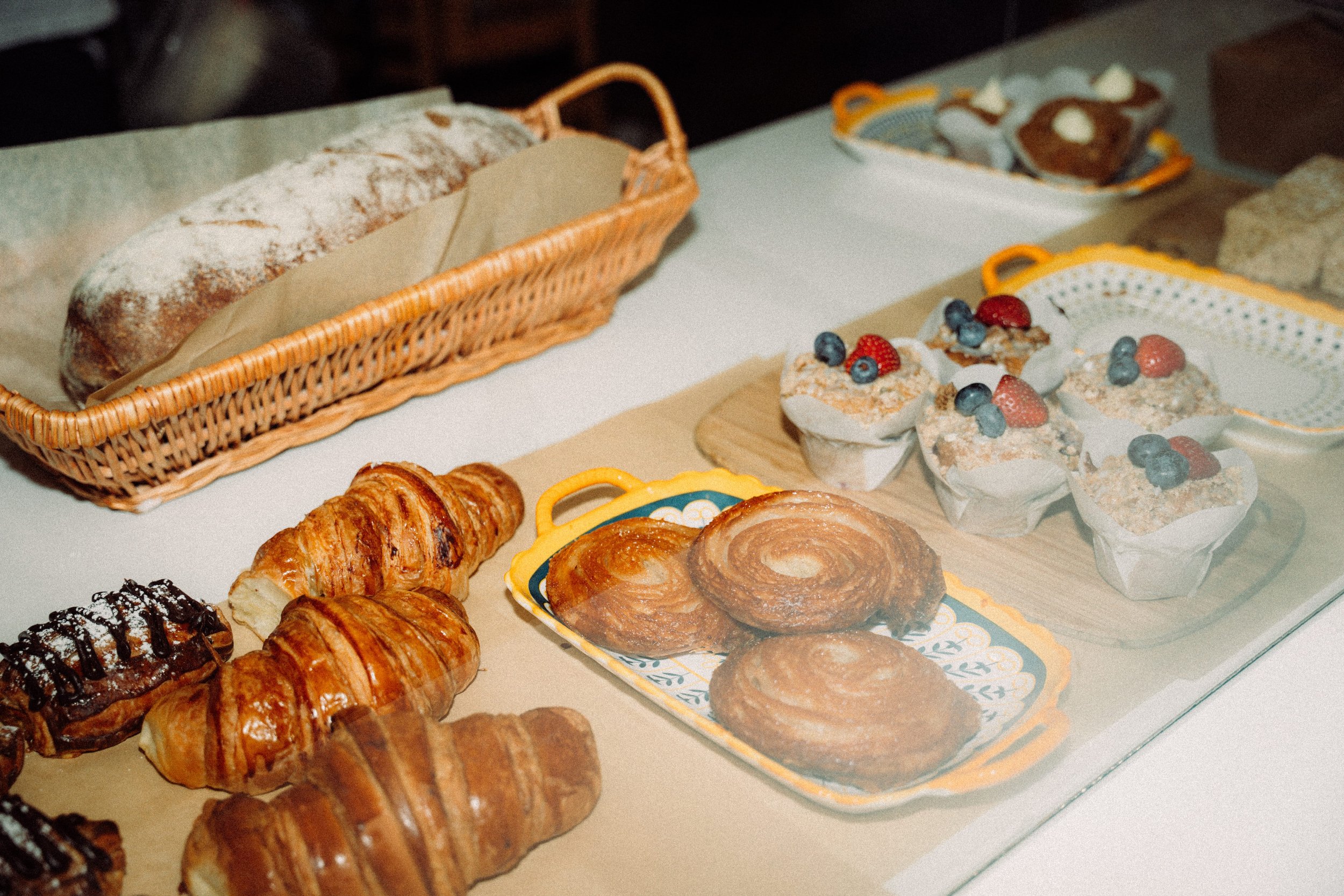 Assorted baked goods including croissants, Danish pastries, and muffins, displayed on a table and in baskets.