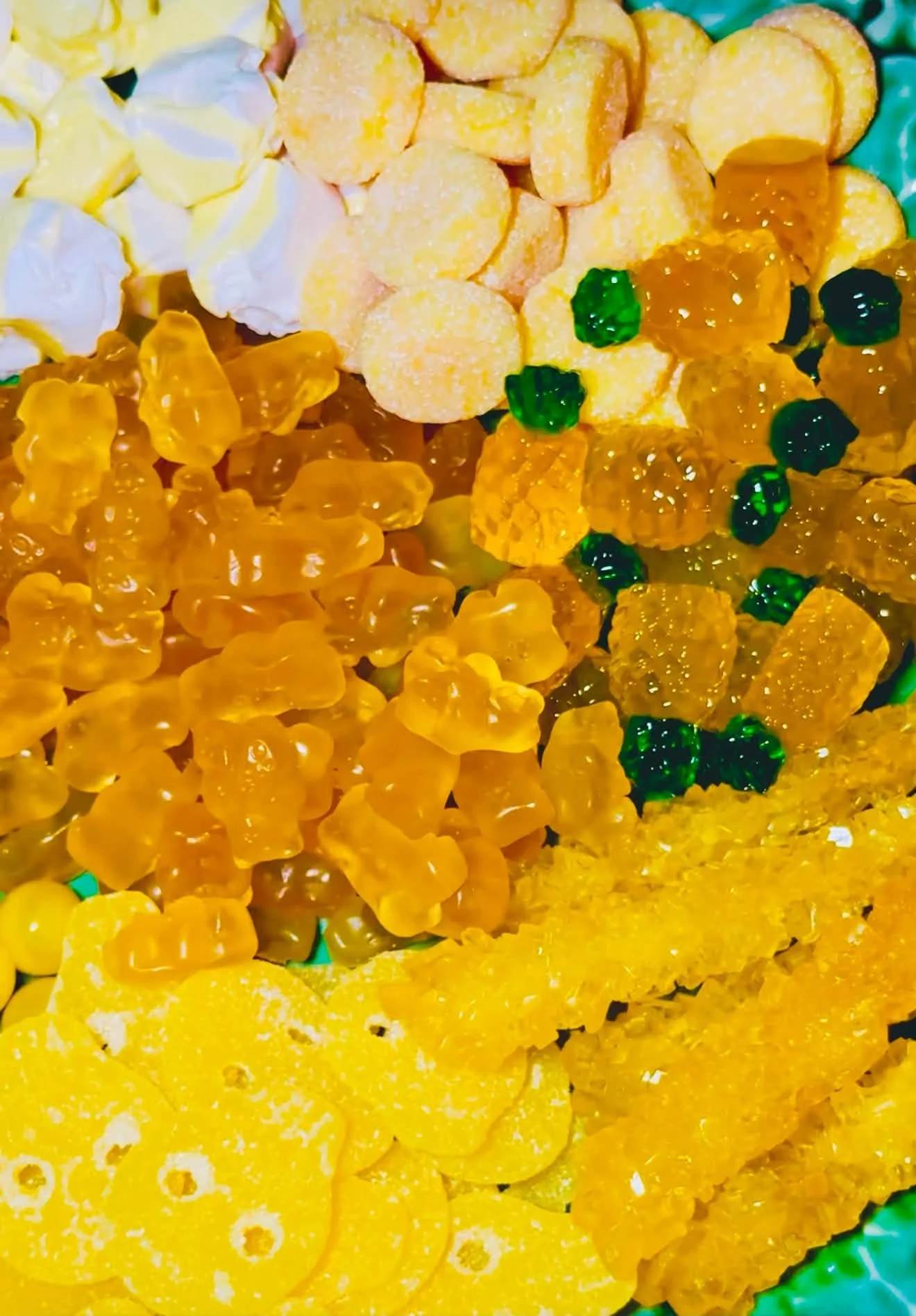 Close-up of various colorful candies, including gummy bears, hard candies, and other sweets in shades of yellow, orange, and green.