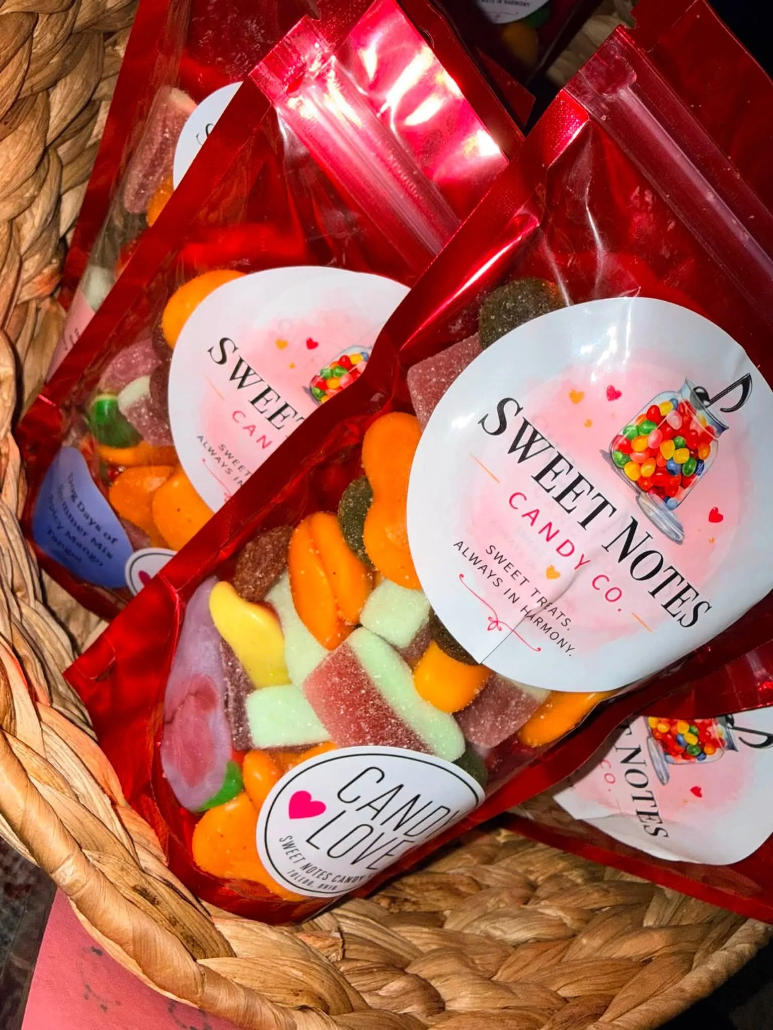 Three red resealable plastic bags of assorted colorful candies inside a woven basket.