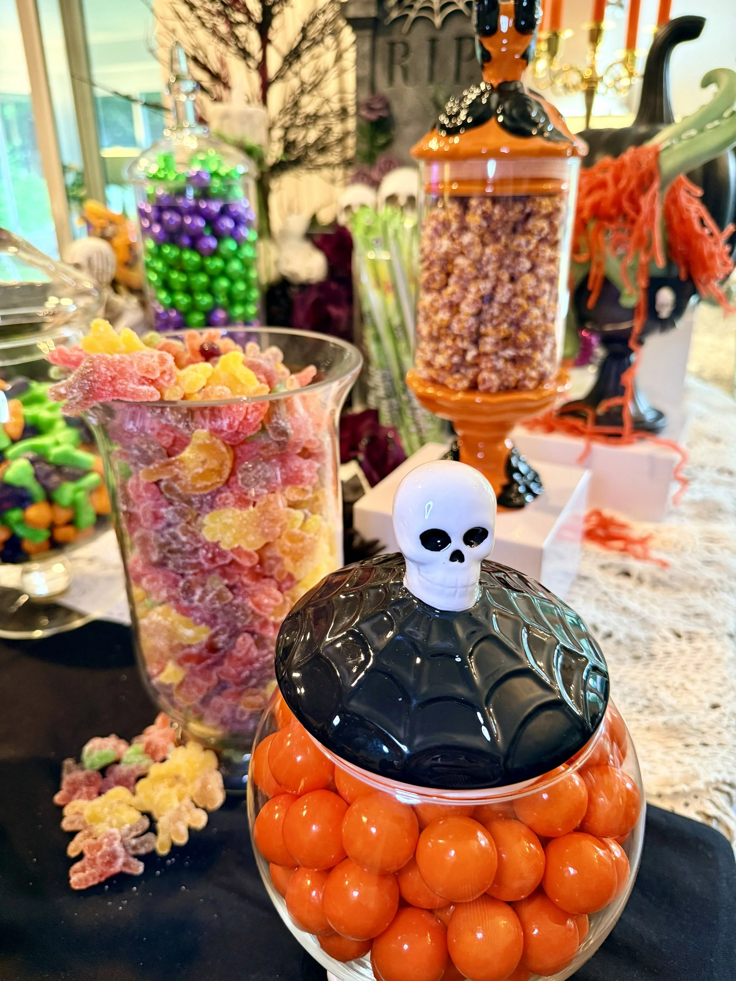 A Halloween-themed candy display with orange, black, and green candies and a skull-shaped container.