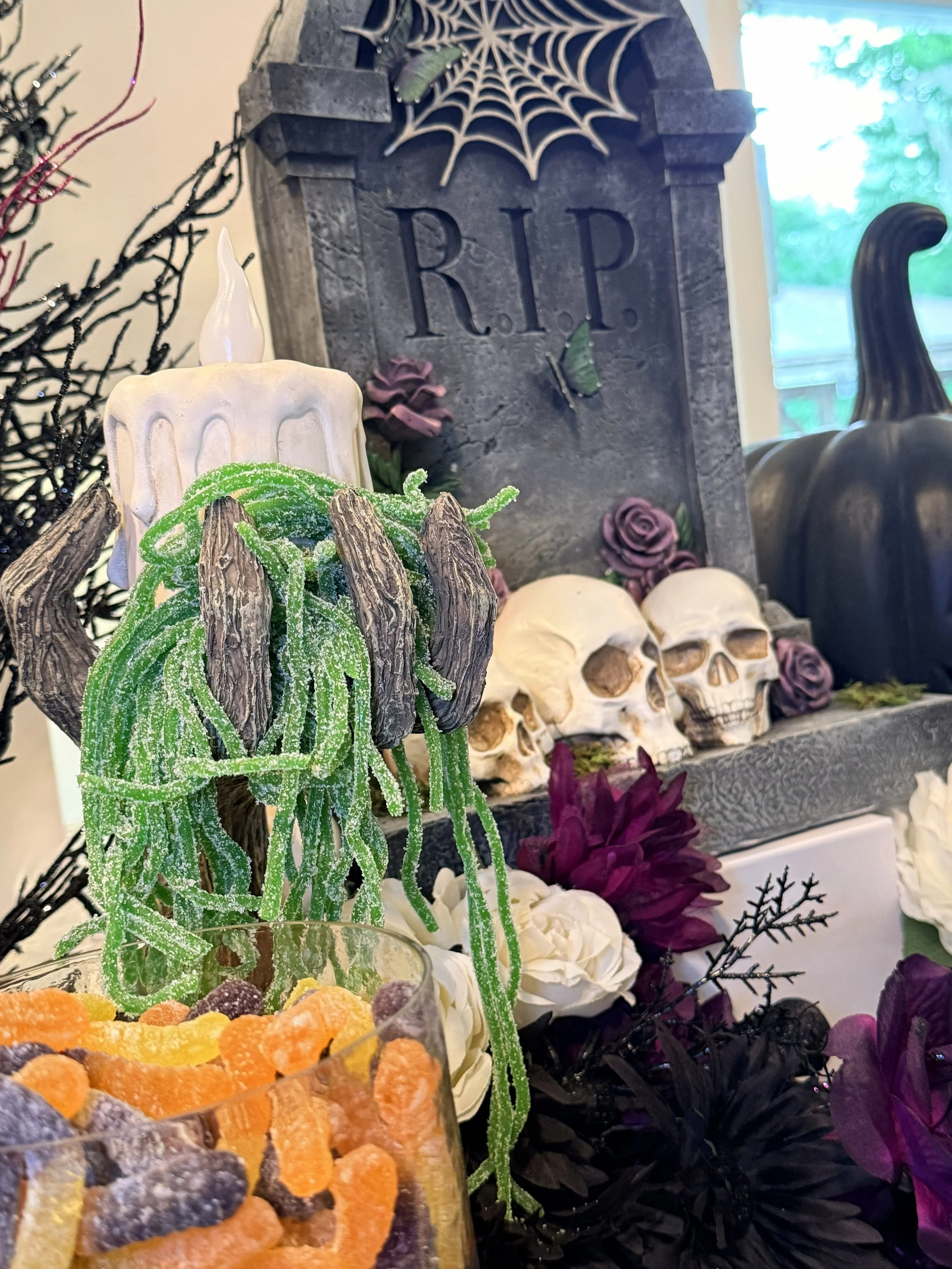 Halloween-themed decoration with skulls, a gravestone with the word 'RIP', a spiderweb, and various artificial flowers.