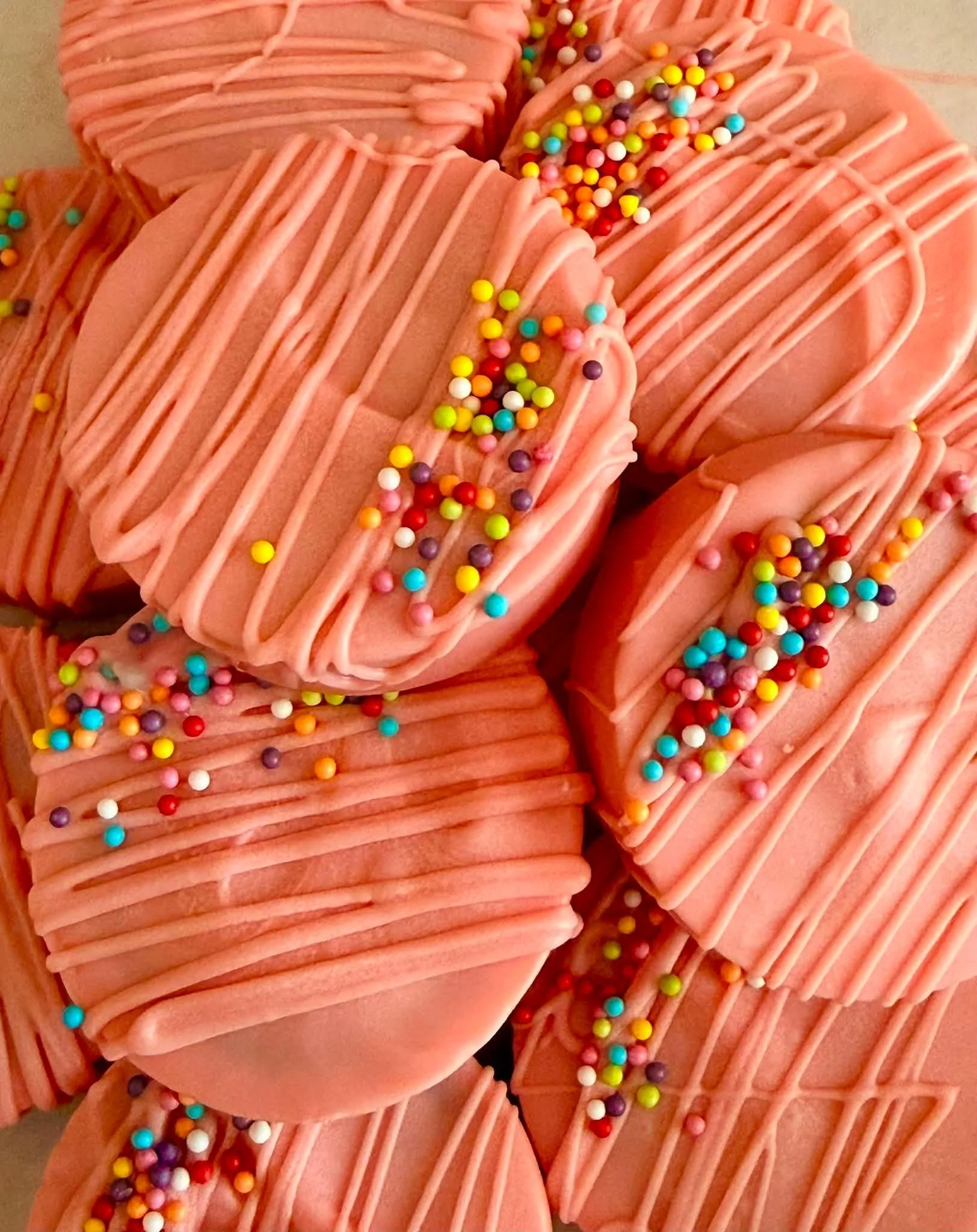 Close-up of pink frosted cookies decorated with colorful sprinkles and pink drizzle.