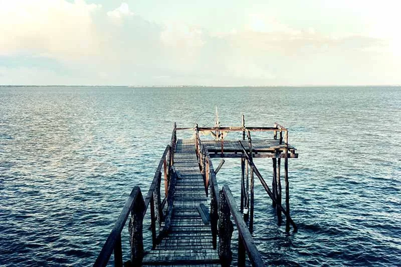A wooden pier stretching out over the calm ocean water with a cloudy sky above.
