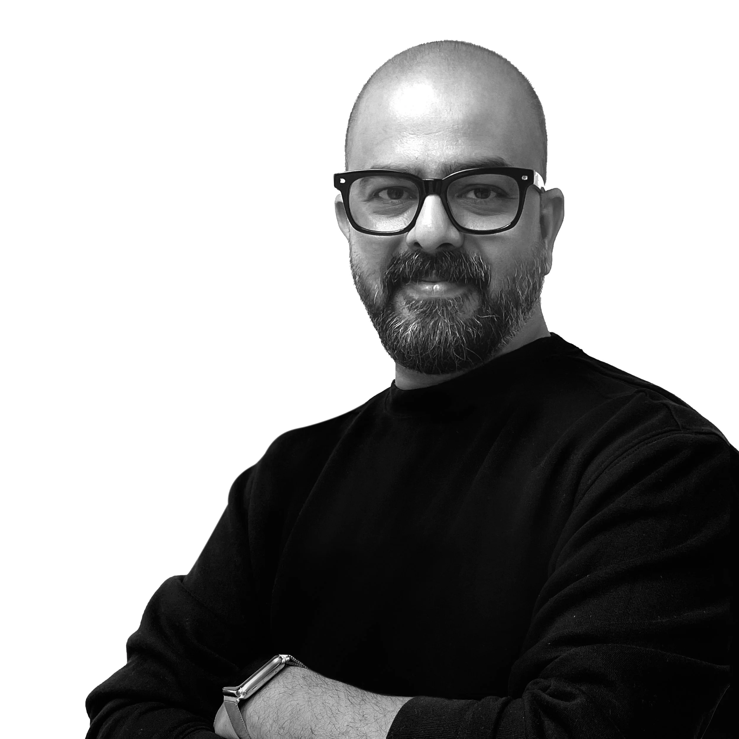A man with a beard and glasses poses with crossed arms, wearing a black shirt and a watch, against a plain background.