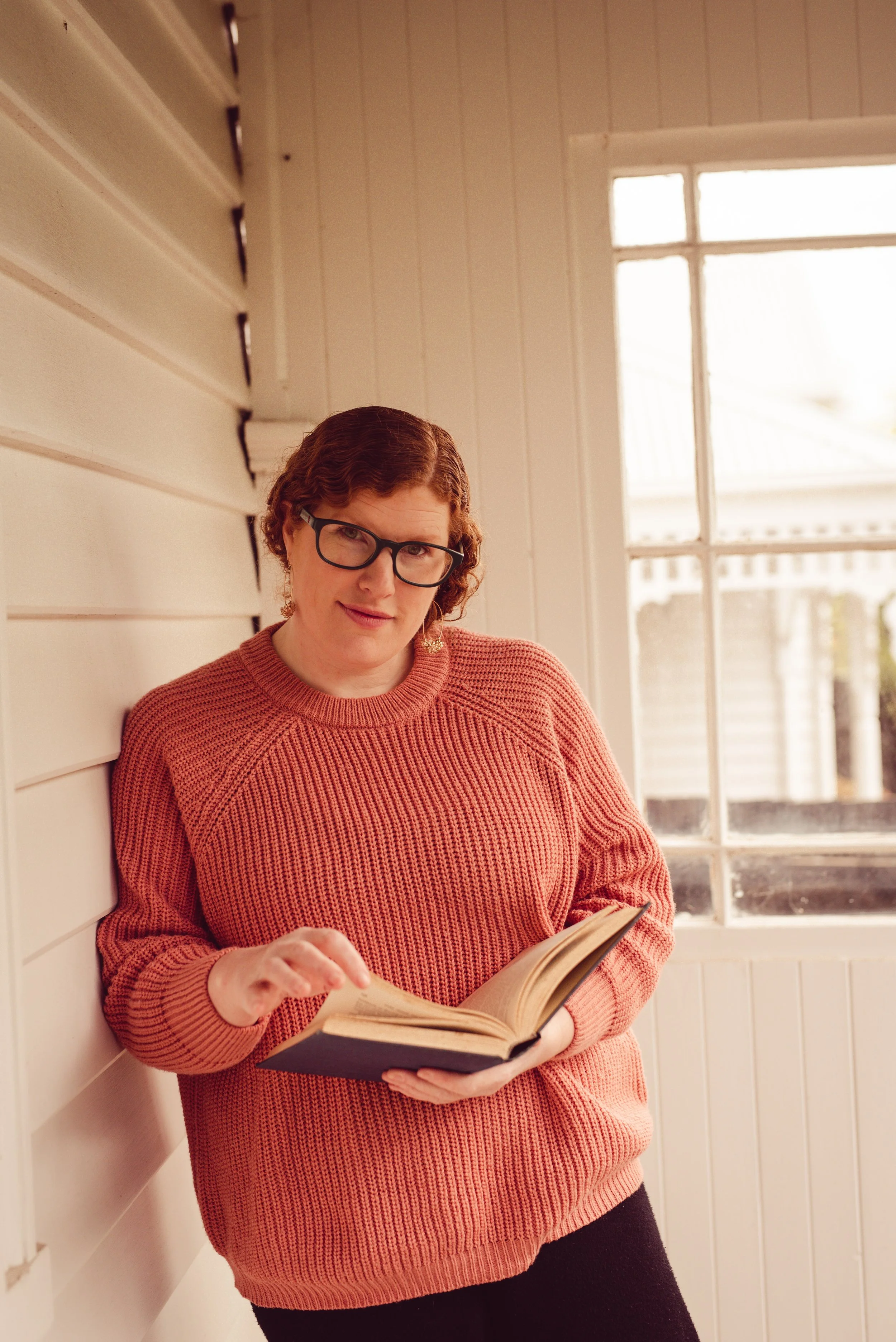 Kristal Leighton standing by a window and reading a book.