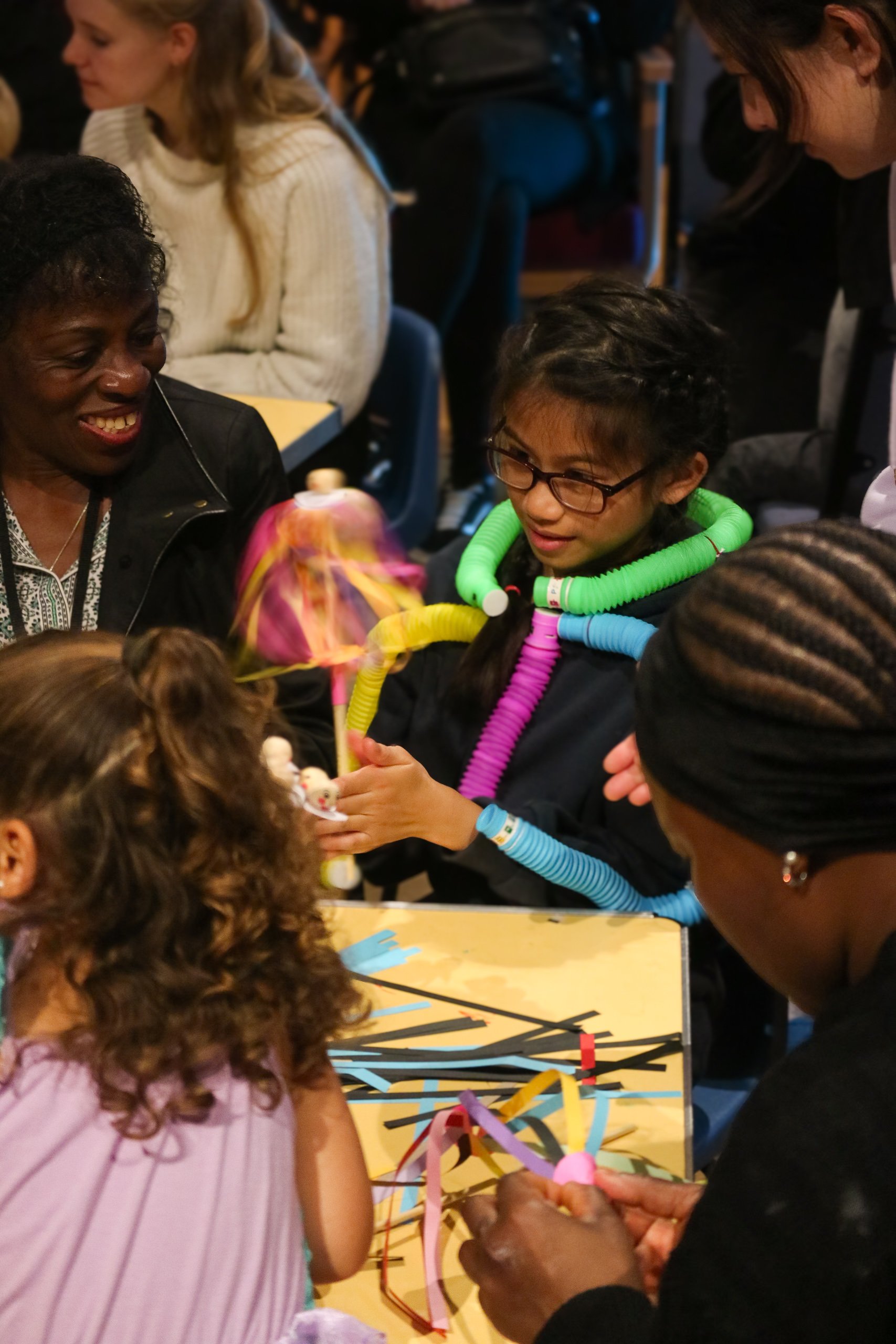 A group of people gathered around a table, exchanging colorful streamers and decorations, in a festive indoor setting.