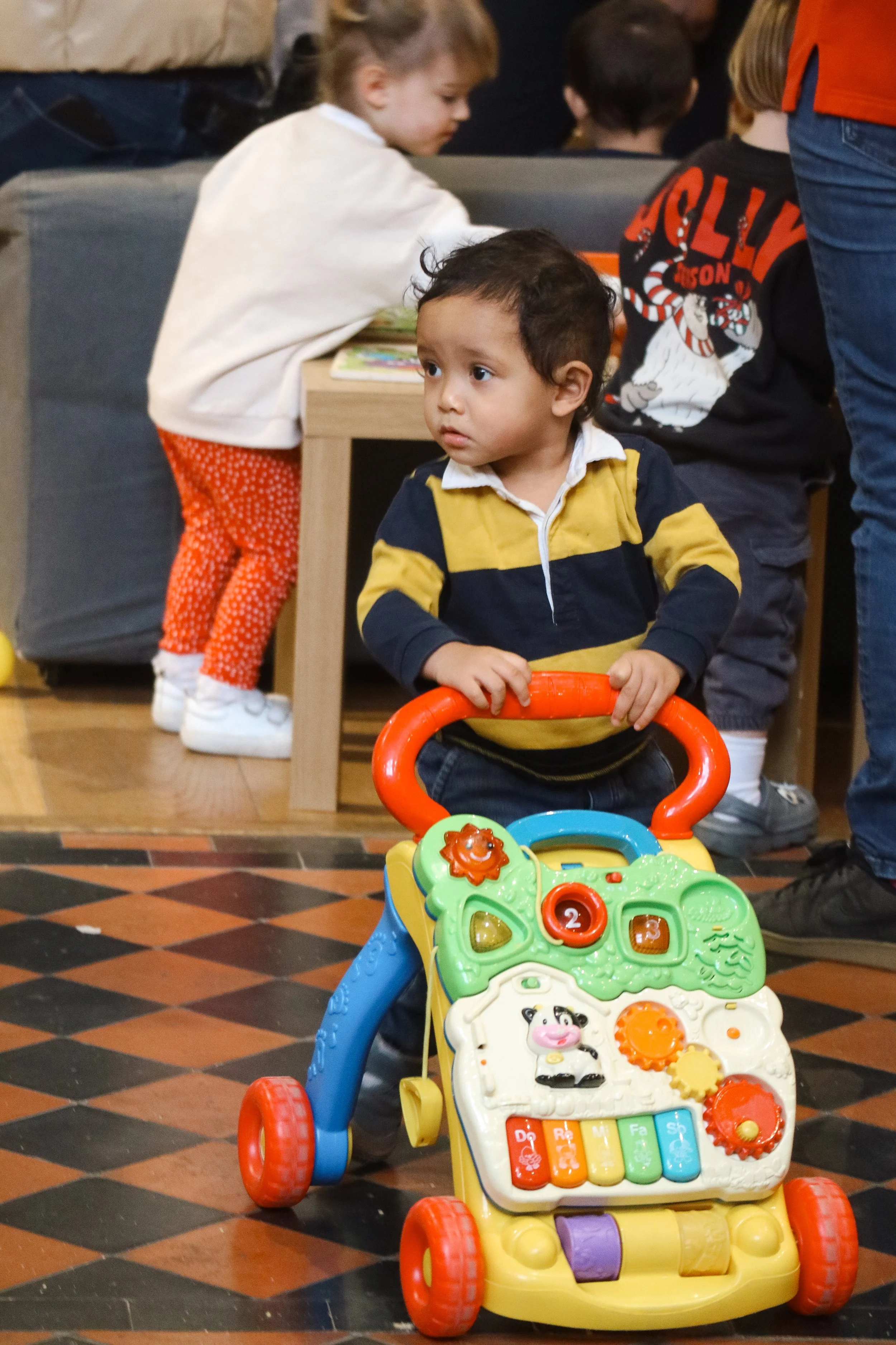 A young boy sitting on a toy walker with colorful animal and alphabet decorations.