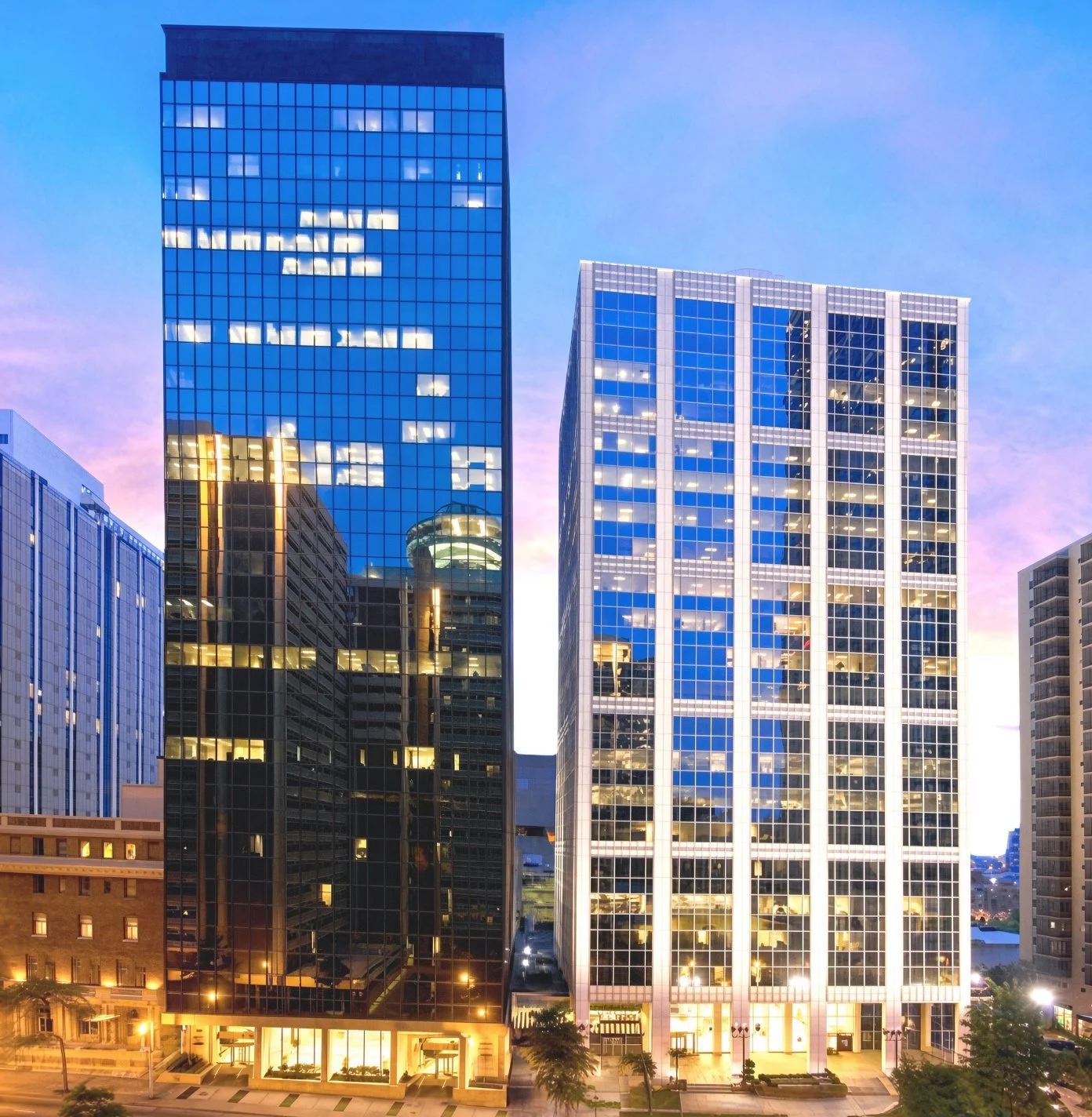 Two modern glass office buildings reflecting the sunset sky in a cityscape.
