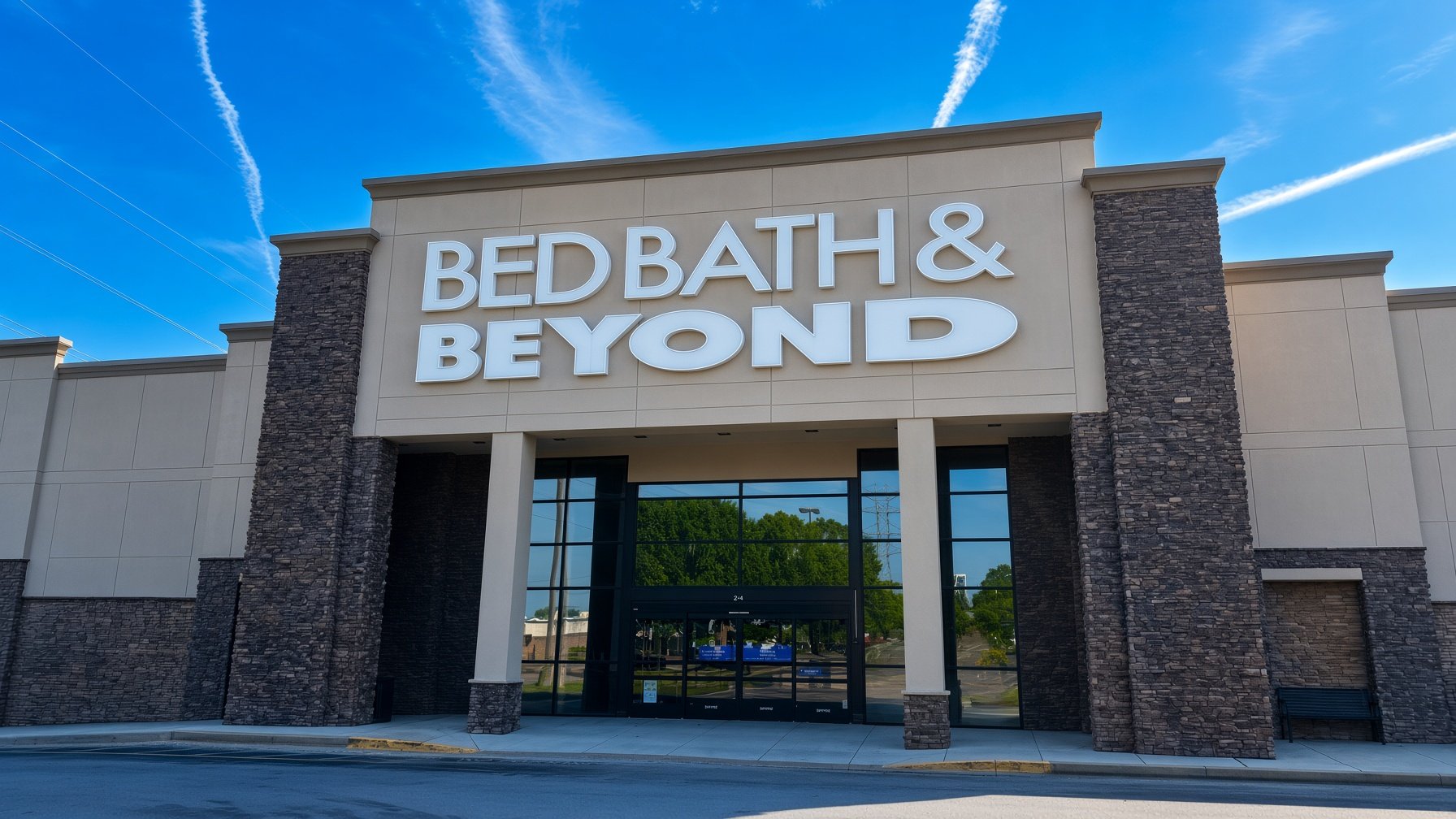 Exterior view of Bed Bath & Beyond store with large sign, stone accents, glass entrance, and blue sky.