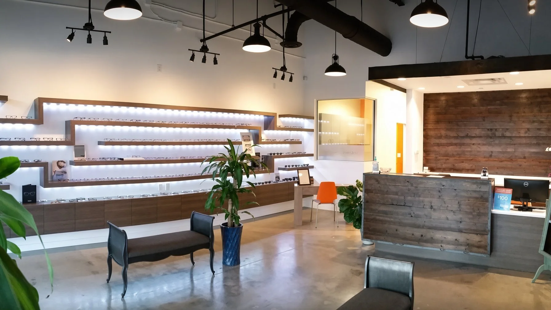 Interior of an eyewear store with white shelves displaying glasses, a reception counter with a computer, a small waiting area with chairs, potted plants, and modern lighting fixtures.
