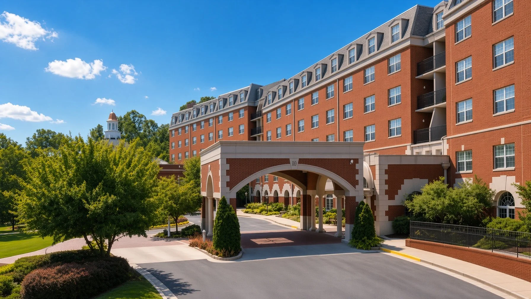 A large brick apartment building with multiple floors, several windows, and a decorative archway entrance surrounded by trees and landscaping.