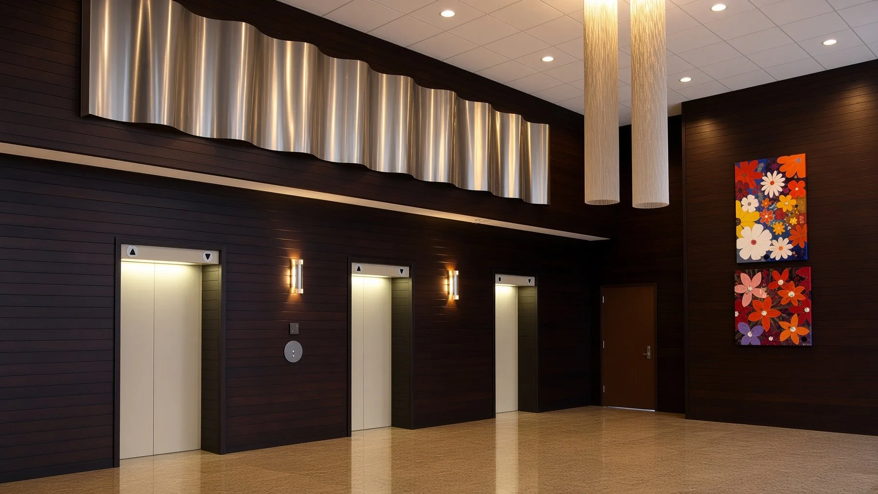A modern interior with three elevator doors on a dark wood-paneled wall, illuminated by wall sconces. Two cylindrical pendant lights hang from the ceiling, and there are colorful floral paintings on the right wall.