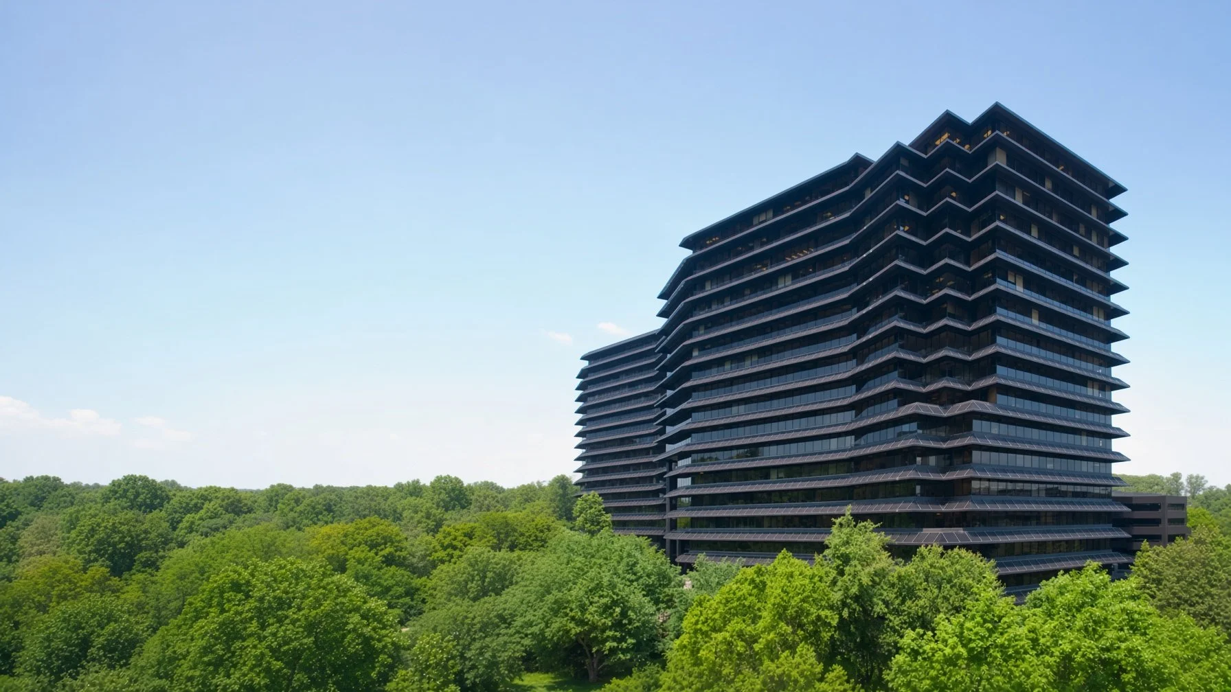 A tall black modern office building with stacked, angular design, surrounded by green trees under a clear blue sky.