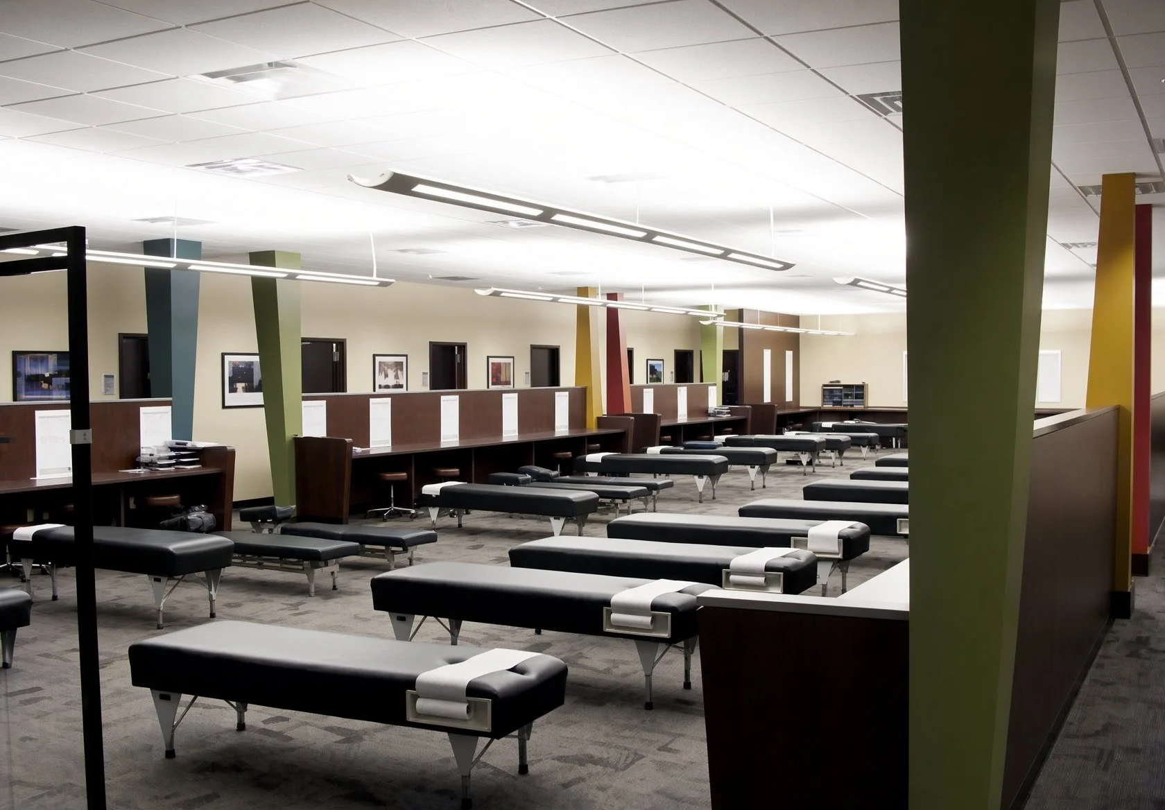 Empty hospital waiting room with black examination tables and green, blue, yellow, and red divider columns.