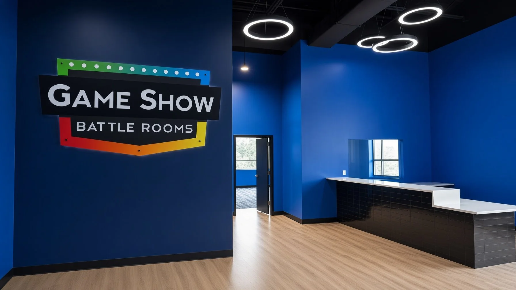 Interior of a gaming center with a large sign that says 'Game Show Battle Rooms' on a blue wall, blue walls, circular ceiling lights, a window, and a reception counter with black tiles and a white top.