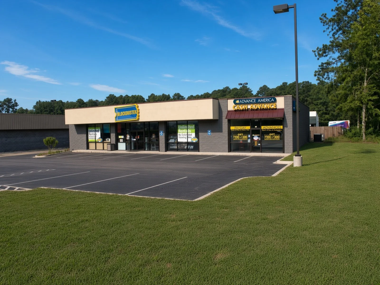 Empty parking lot in front of a Blockbuster store with signs for payday loan services, under a blue sky with a few clouds.