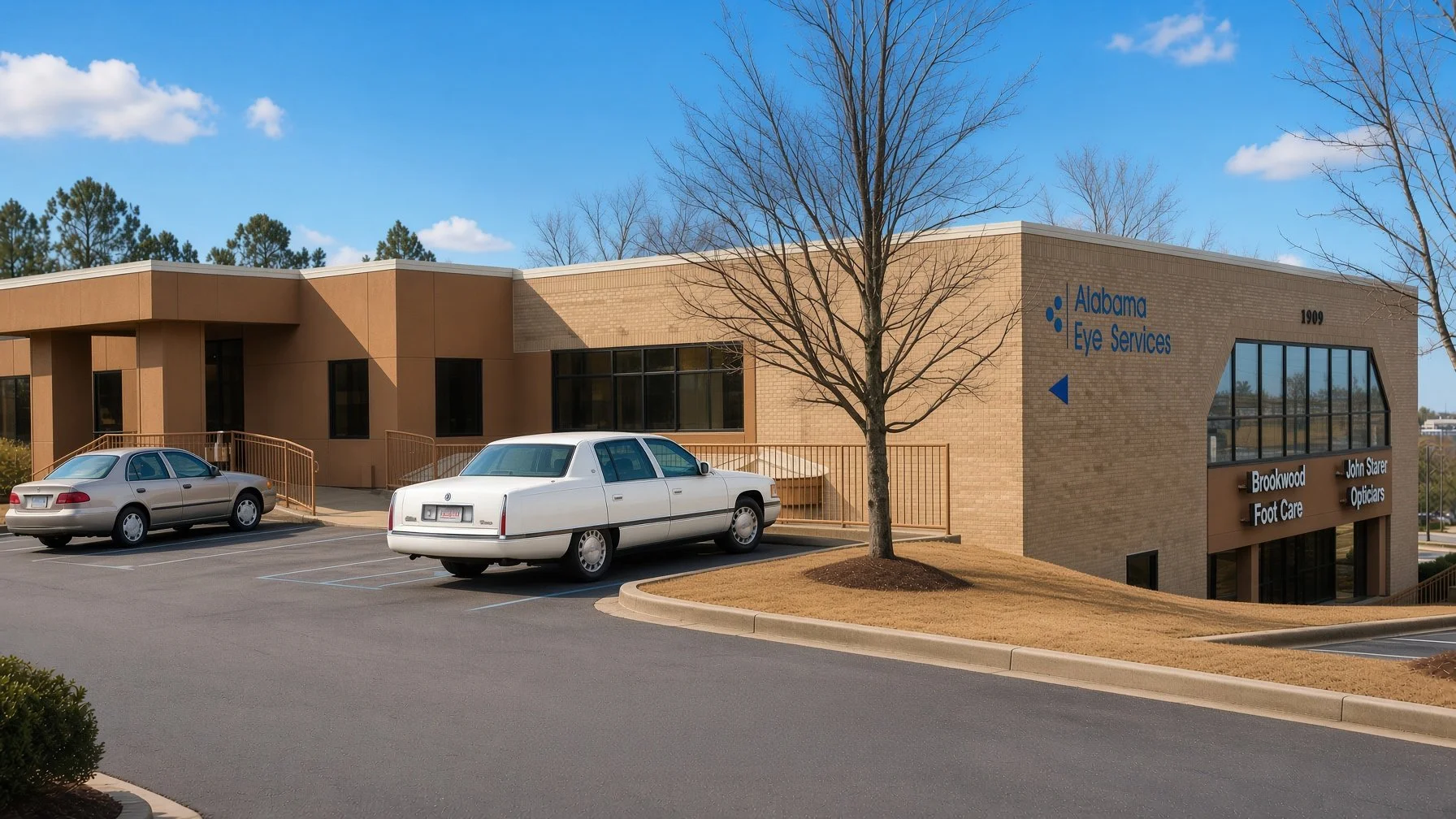 Exterior view of Alabama Eye Services building with parking lot in front, two parked cars, leafless trees, clear sky, and signage for eye care services.