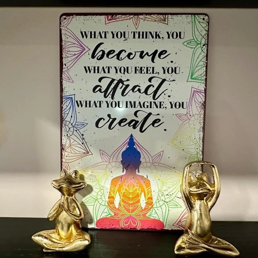 Decorative sign with inspirational quote, Buddha silhouette, and two gold animal figurines on a black surface.