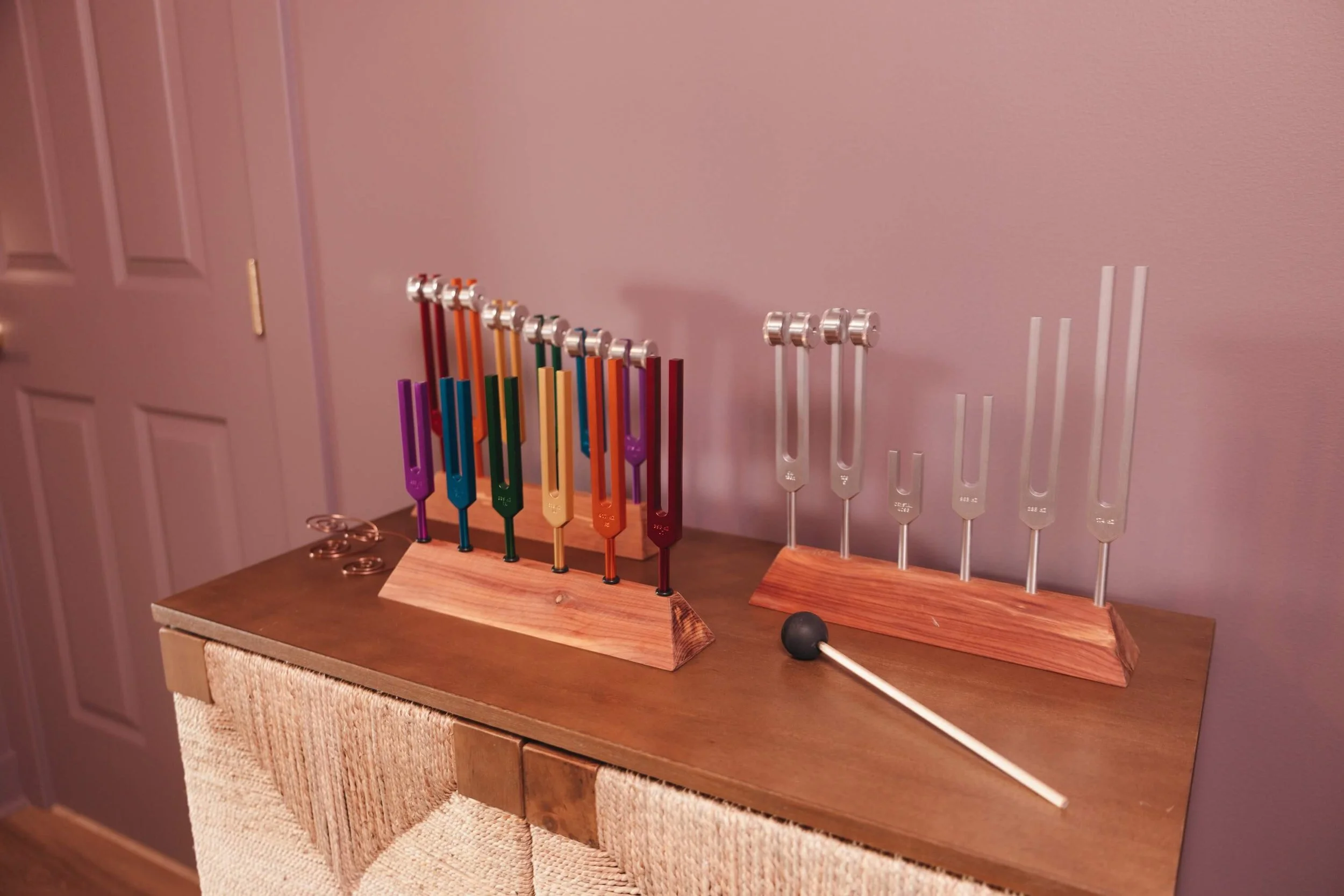 Two wooden stands holding colorful tuning forks on a wooden table against a pink wall.