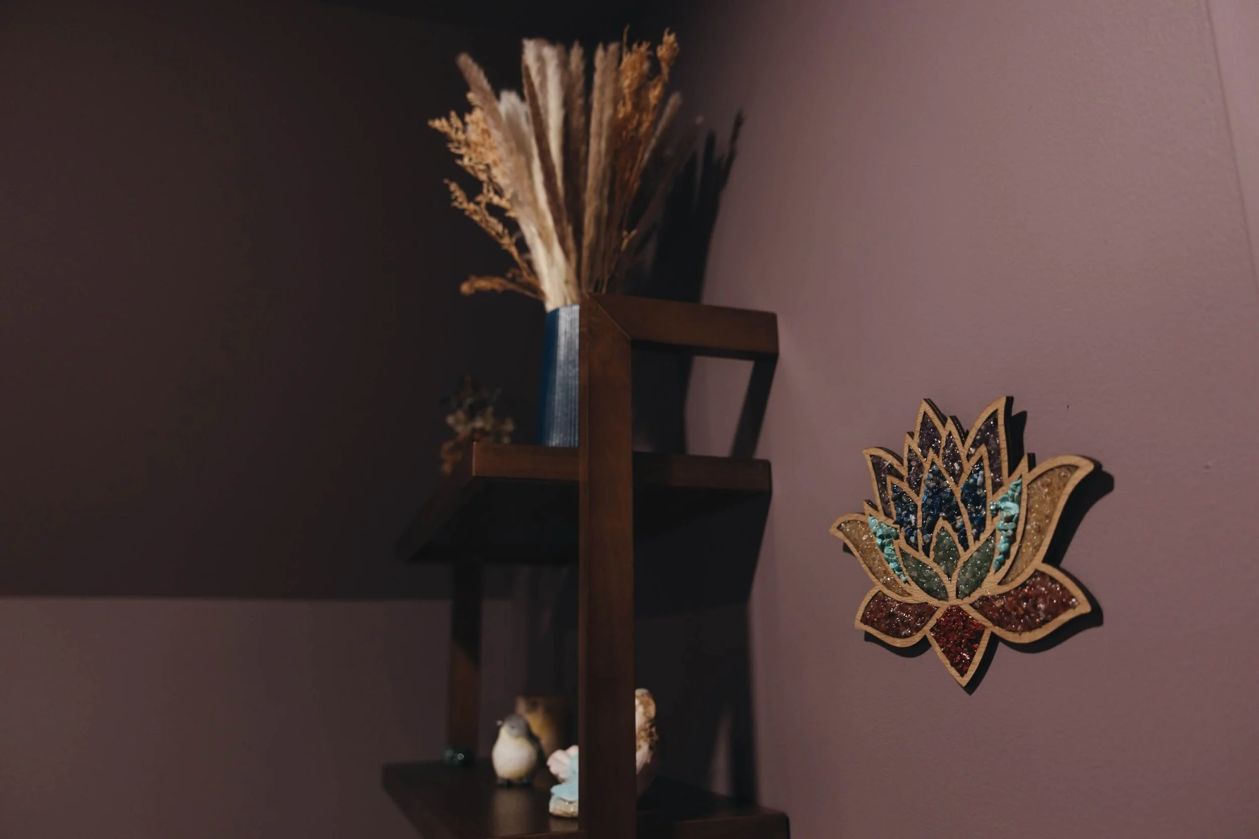 A dark wooden wall shelf displaying decorative items and a colorful decorative lotus flower wall hanging.