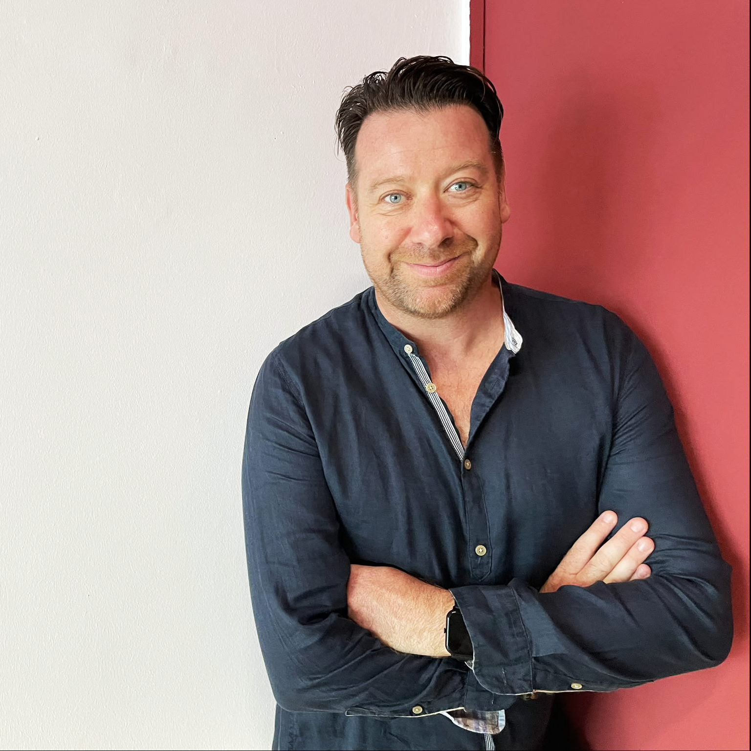A man with crossed arms, smiling, standing against a wall with one side white and the other painted red.