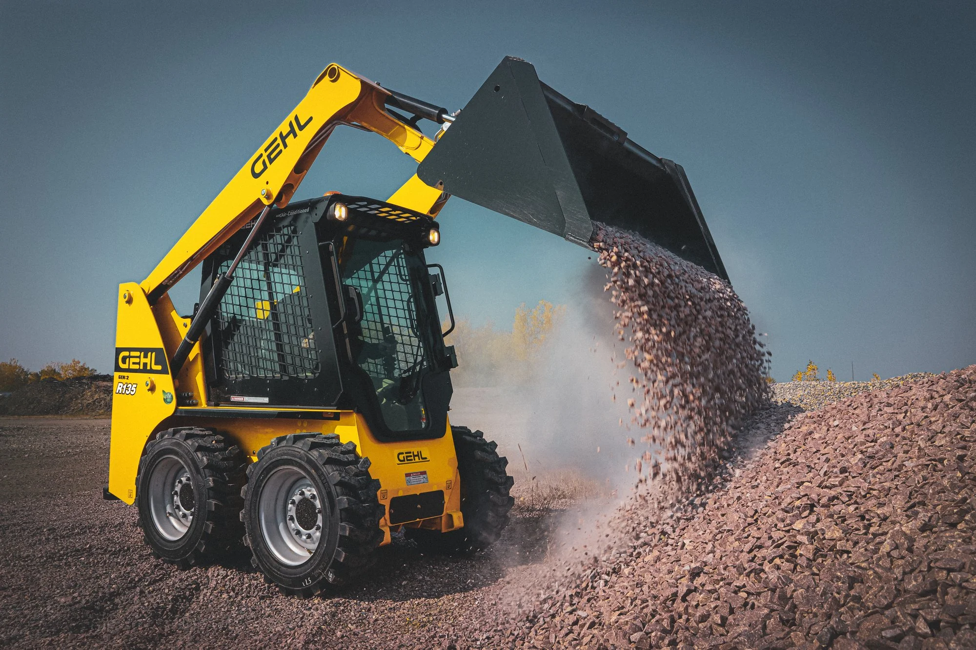 A yellow construction loader dumping dirt and rocks onto a pile on a construction site under a clear blue sky.