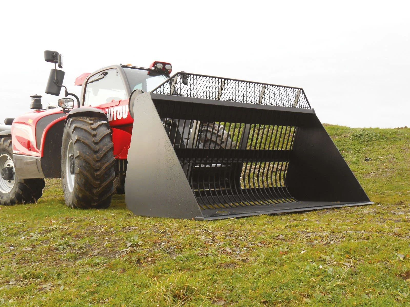 A red tractor with a black front loader attachment on grassy ground.