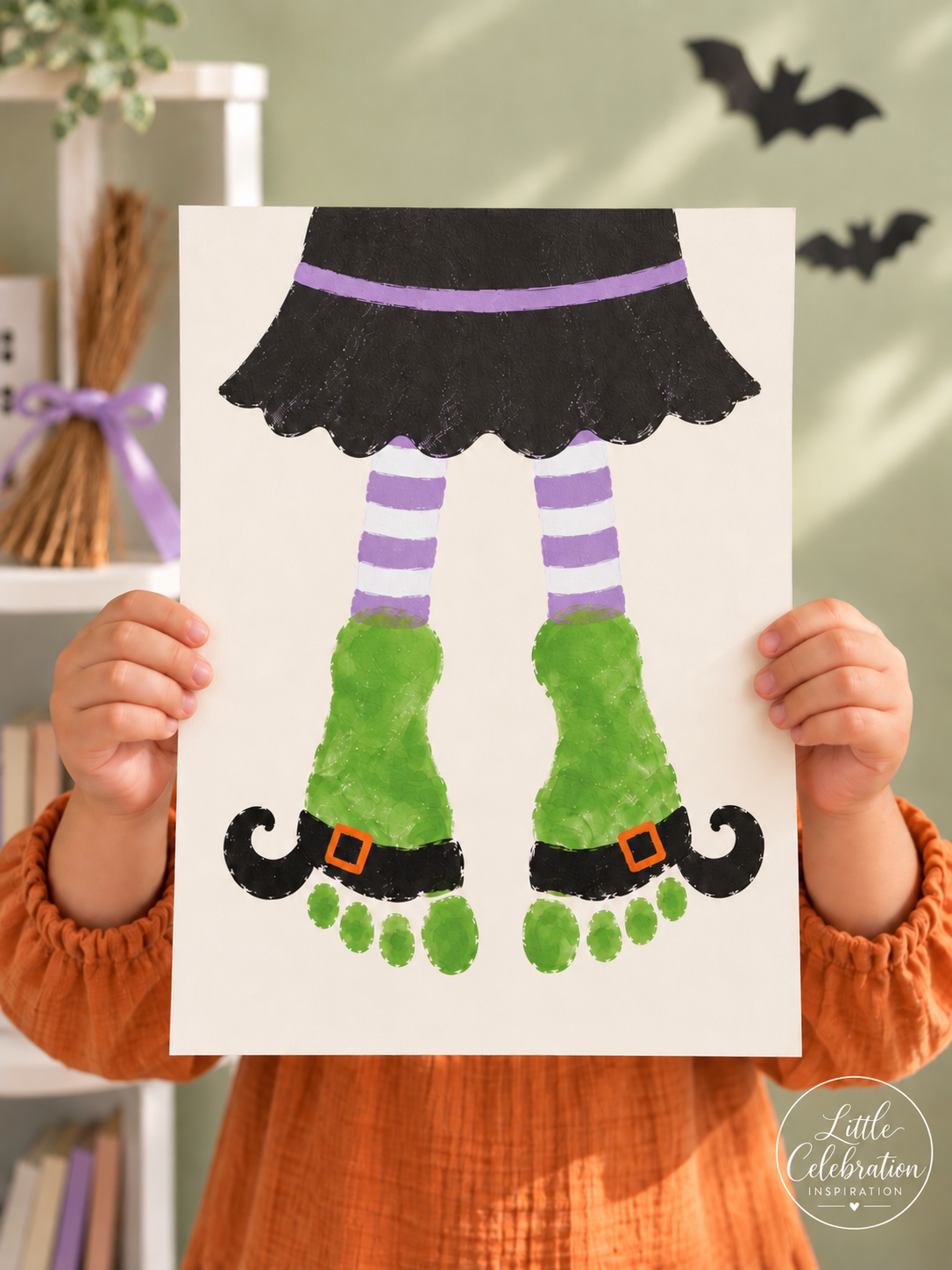 Child holding a Halloween keepsake made from two green footprints decorated as witch legs and shoes.