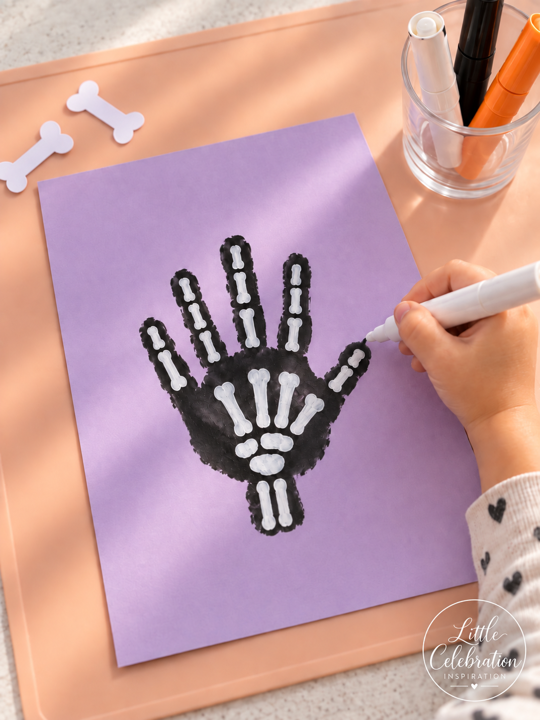 Black toddler handprint with white painted skeleton bones on lavender cardstock.