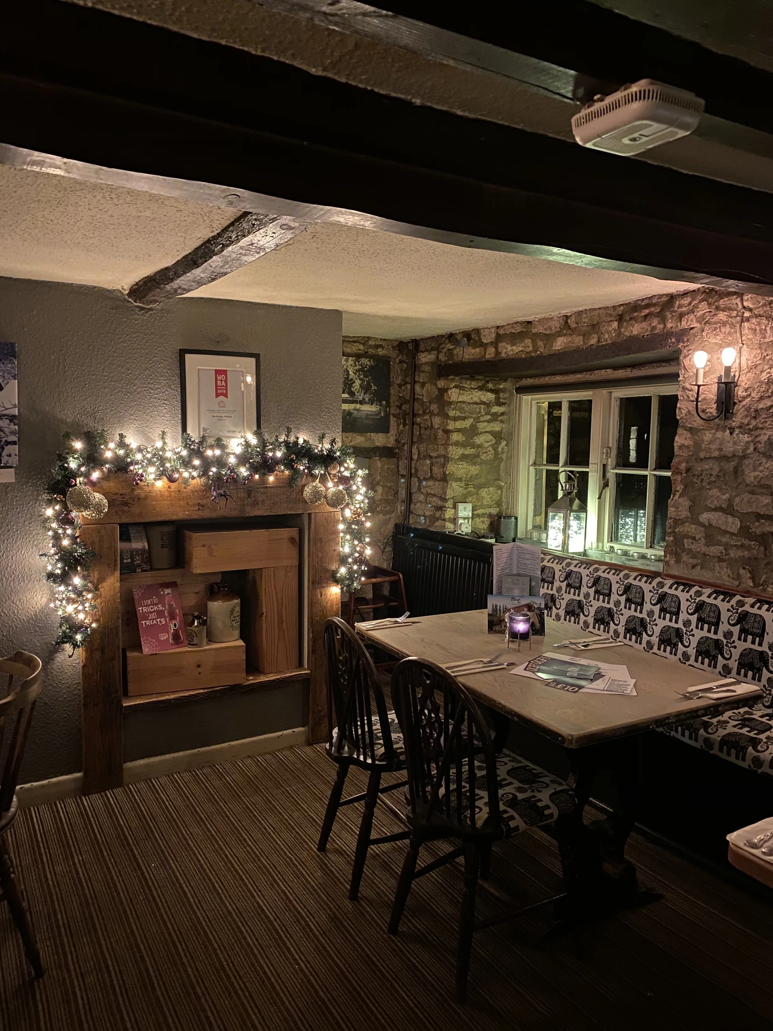 Cozy restaurant with a decorated fireplace and dining table, lit by candlelight, Christmas decorations, and warm lighting.