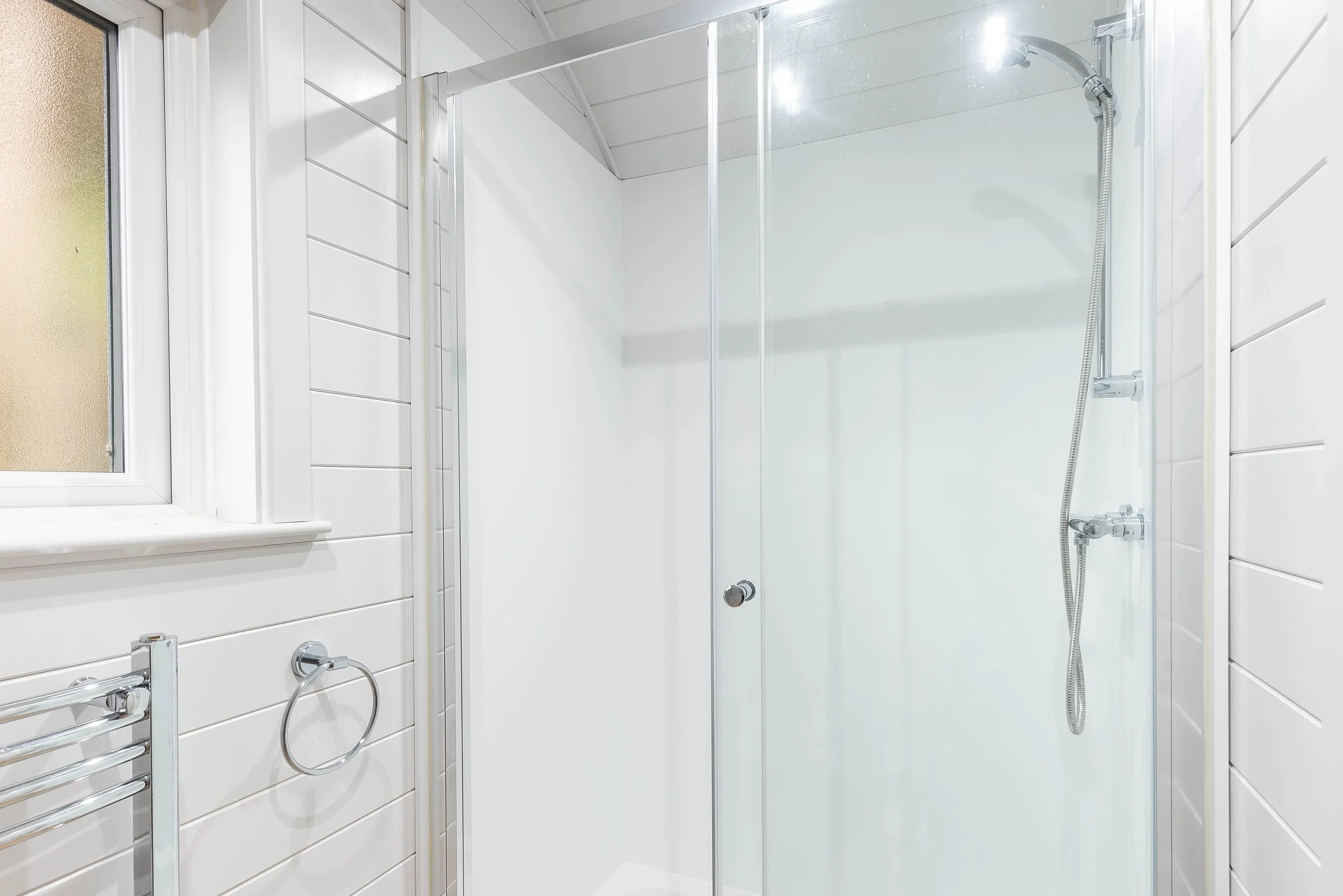 A modern bathroom shower with white tiled walls, a glass door, and a handheld showerhead.