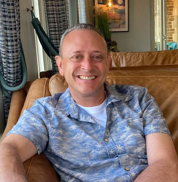 Photo of David Bower sitting on a sofa smiling
