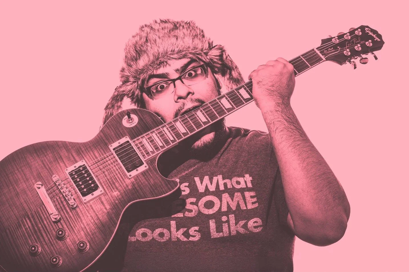 A man with glasses, a furry hat, and a beard holds an electric guitar with a pink background.