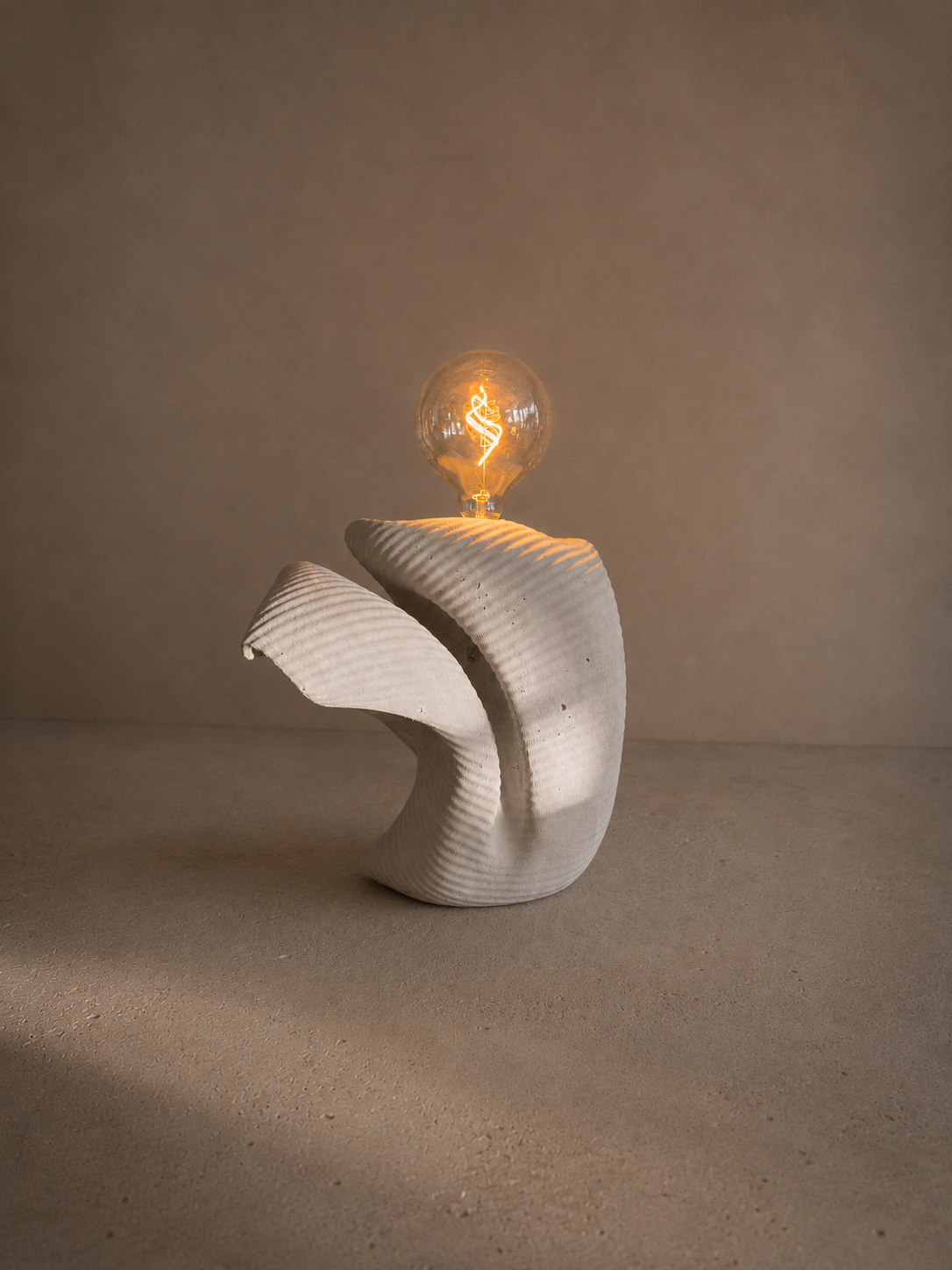 A modern decorative sculpture with a curved, textured white base and a glowing vintage-style light bulb on top, set on a plain surface against a neutral background.