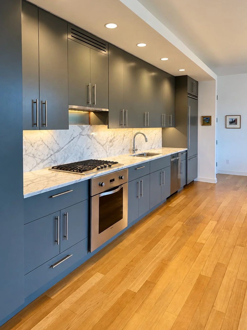 Modern kitchen with gray cabinets, marble backsplash, stainless steel appliances, wooden floor, and recessed ceiling lights.