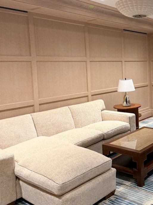 Living room with beige sectional sofa, wooden coffee table, side table, and a table lamp against a paneled wall.