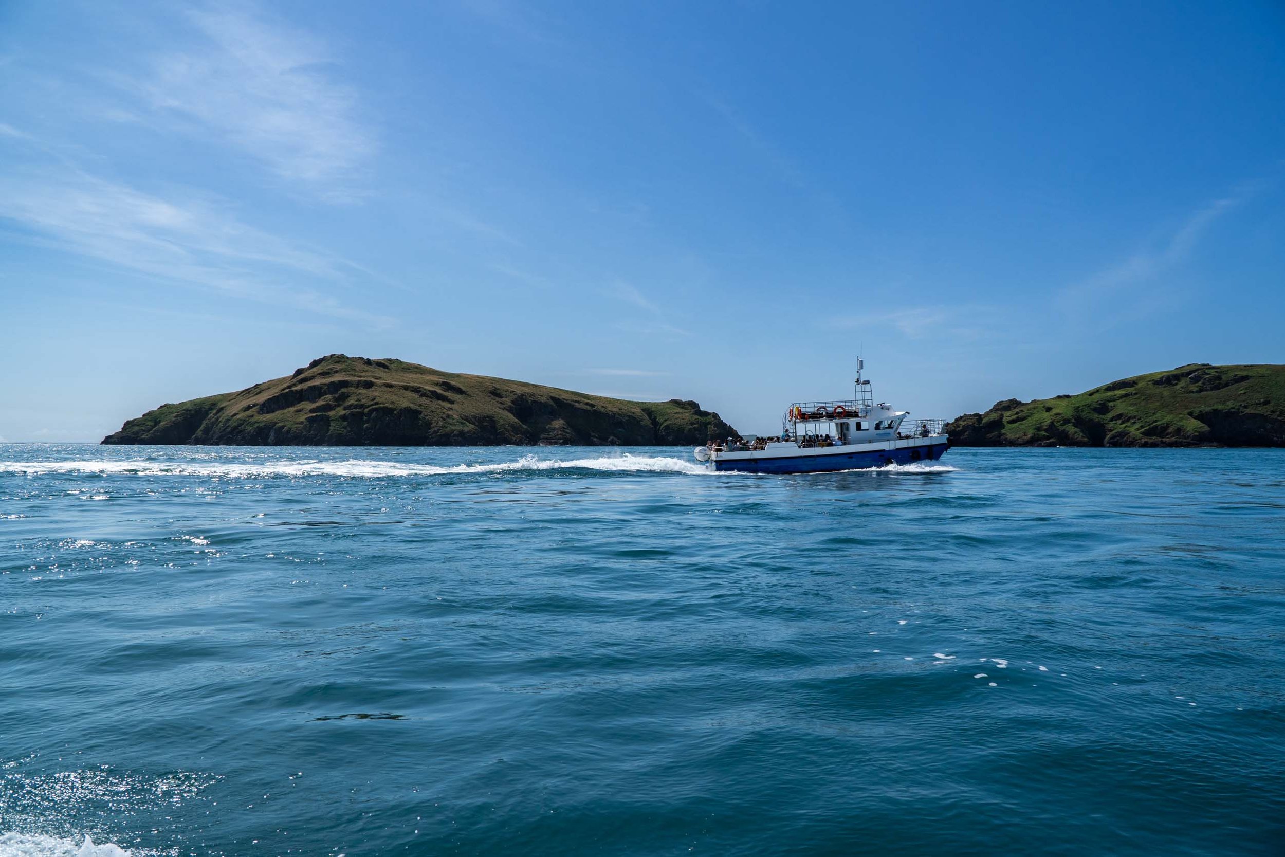 A boat cruising through blue ocean water near green, rocky islands under a partly cloudy sky.