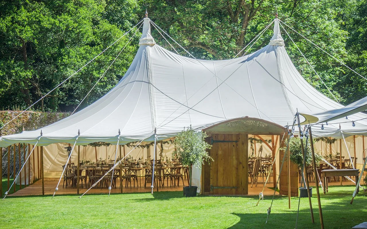 Outdoor wedding marquee with wooden floor, decorated with greenery, set up with tables and chairs, surrounded ancient walls and Woodland.