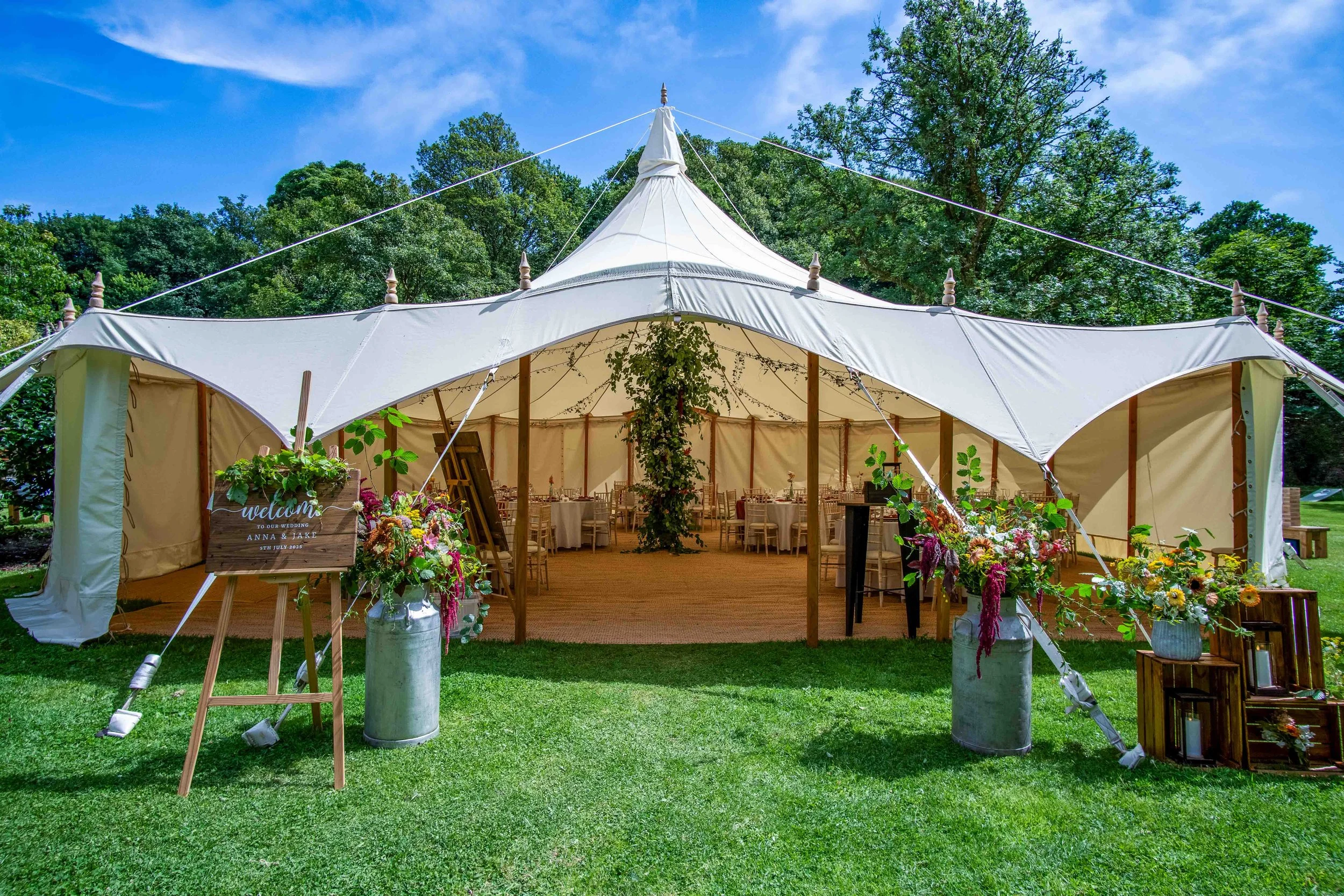 Wedding tent decorated with flowers and greenery on a grassy lawn under a blue sky.