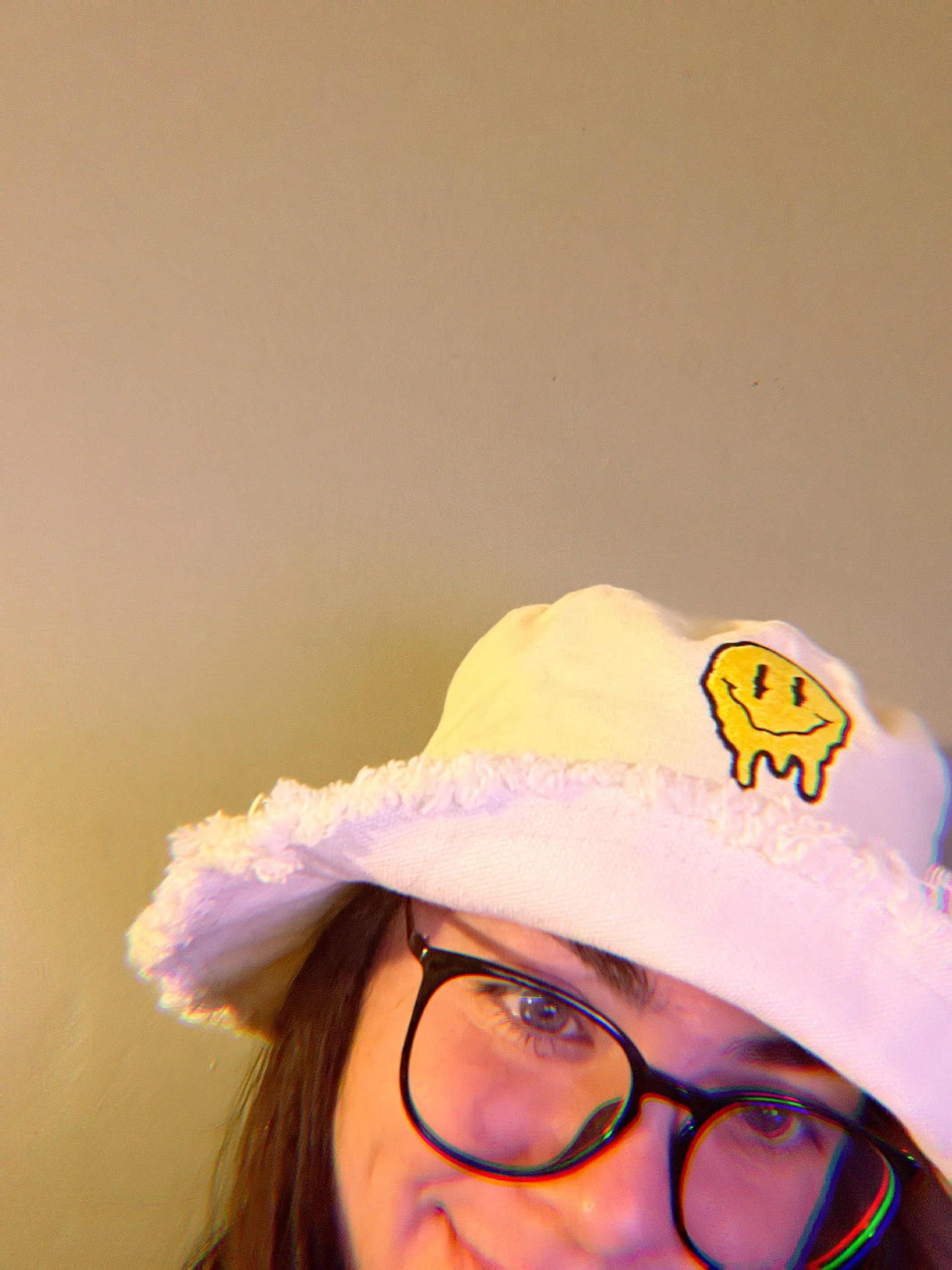 Close-up of a woman with glasses wearing a white hat with a smiley face design.