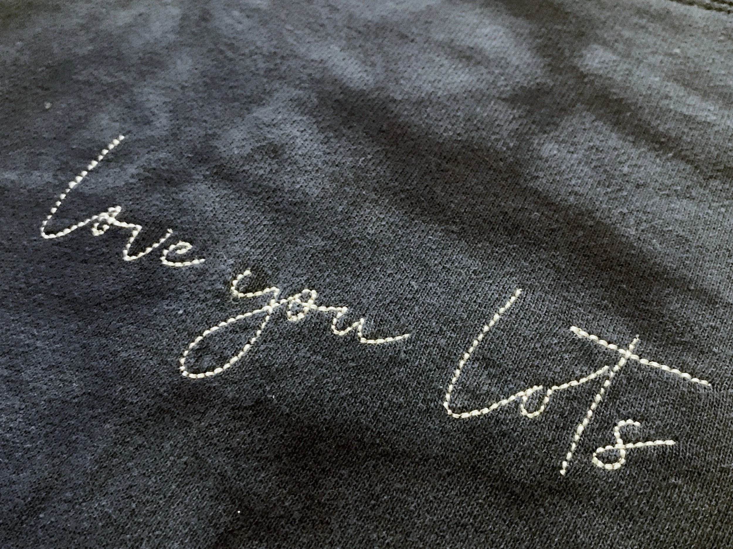 Close-up of black fabric with white embroidered cursive text.