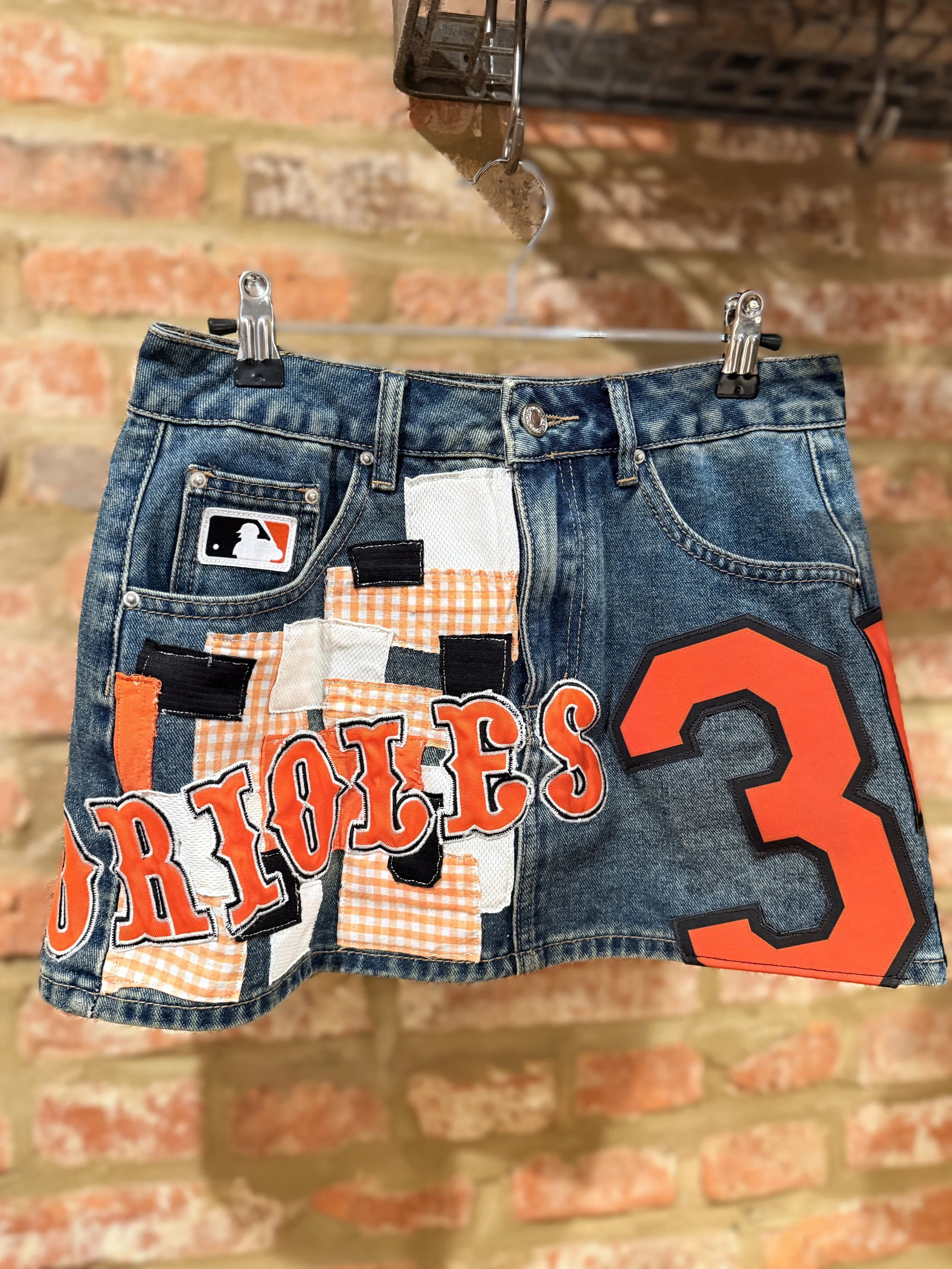 A skirt customized with orioles design handing in front of a brick wall.