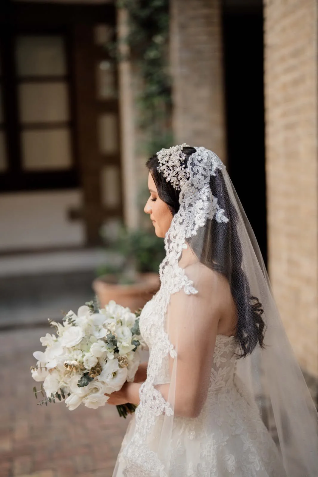 Novia sujetando ramo de novia blanco con orquídeas y follaje de eucalipto sobre fondo claro