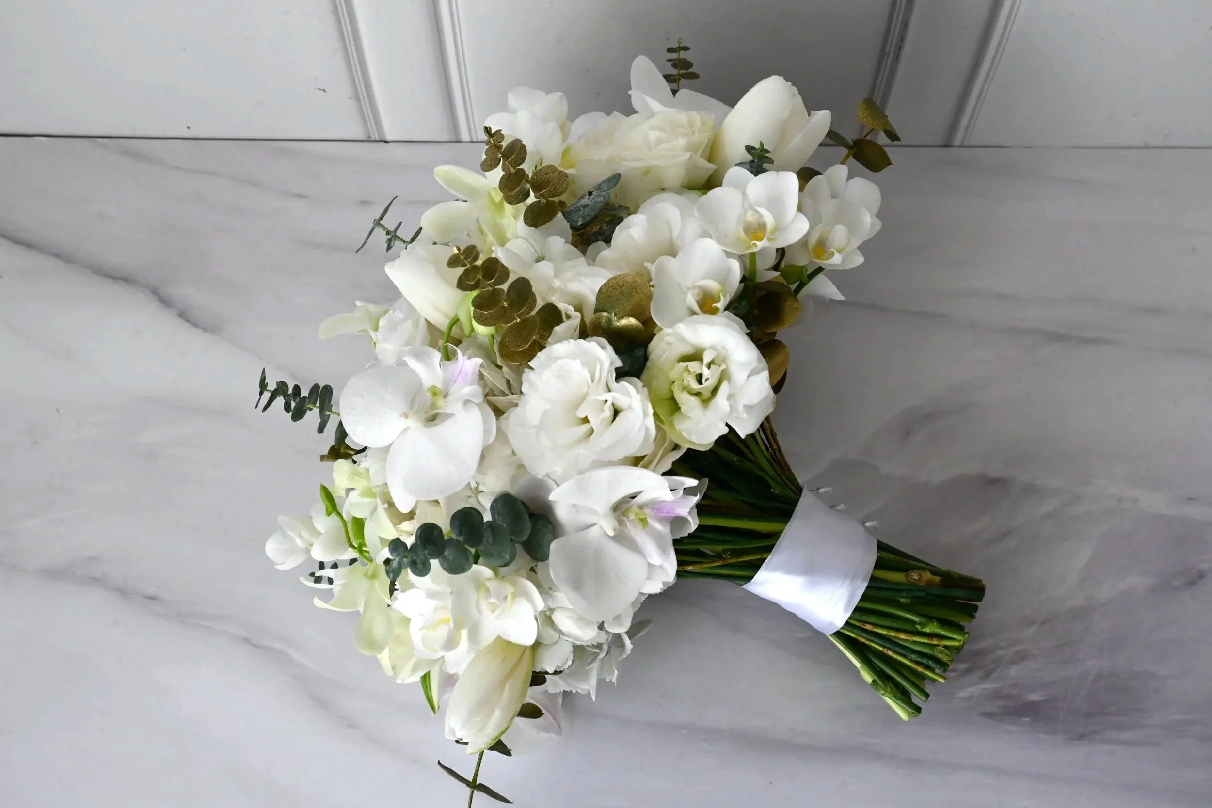 Ramo de novia blanco con orquídeas y follaje de eucalipto sobre fondo claro