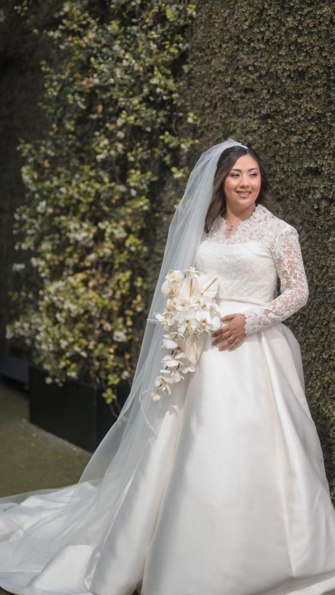 Novia caminando al aire libre con vestido de satén y ramo de novia blanco