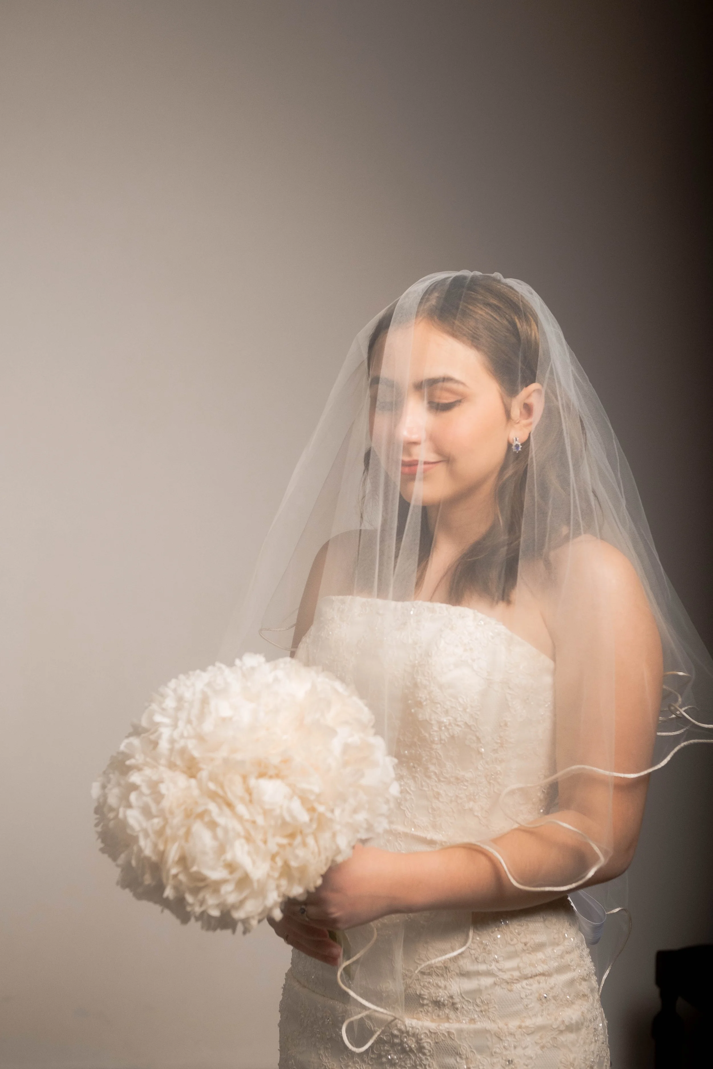 Novia bajo el velo sosteniendo un ramo clásico de peonías blancas