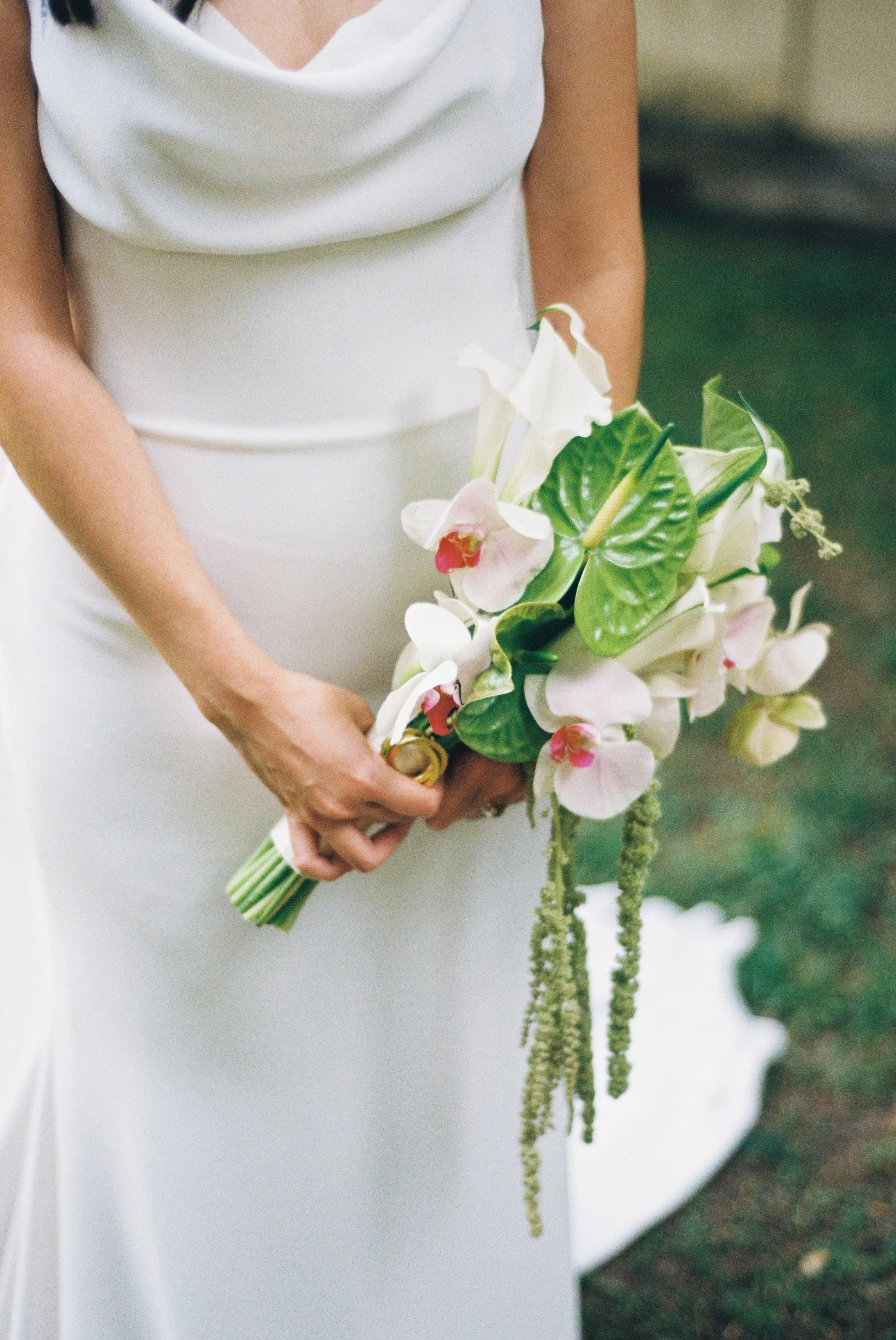 Novia con ramo editorial de orquídeas blancas, anturios verdes y amaranto colgante