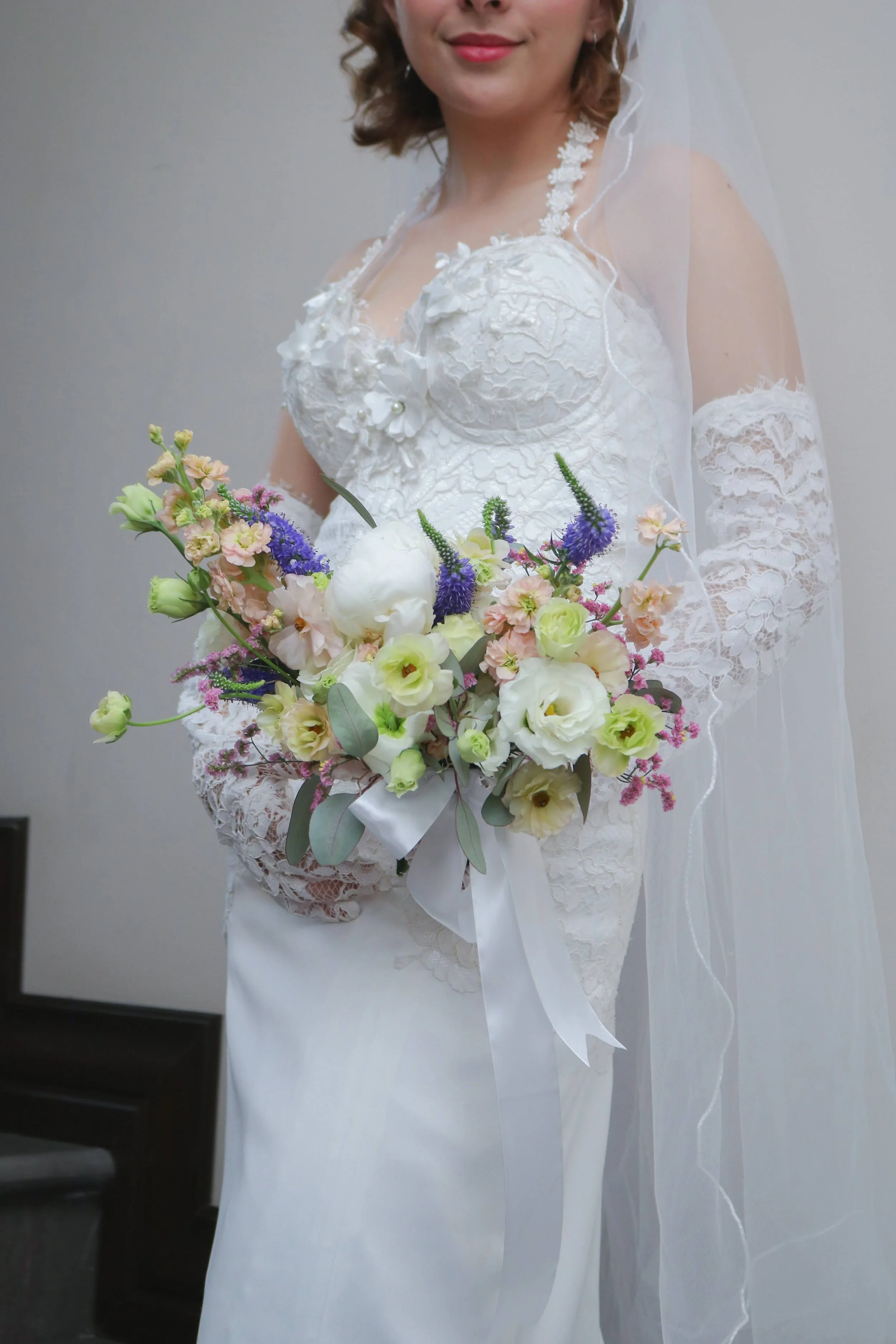 Novia sosteniendo un ramo orgánico de flores blancas, lilas y azules con listones