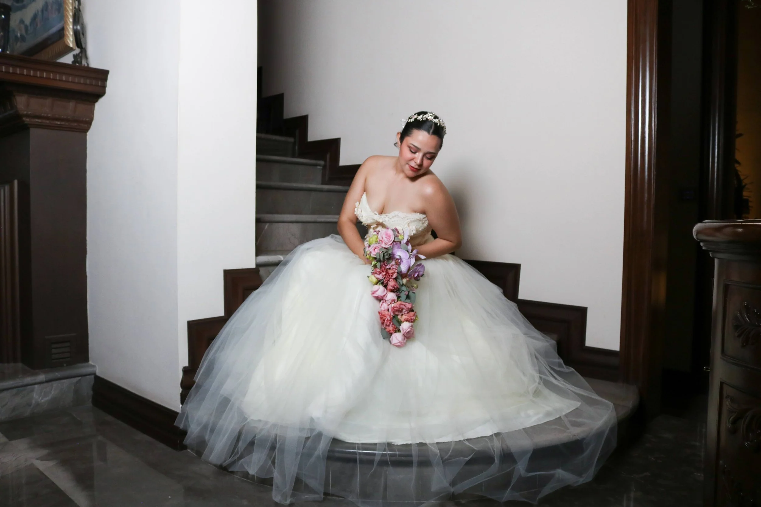 Novia sentada en una escalera sosteniendo un ramo en cascada rosa y morado